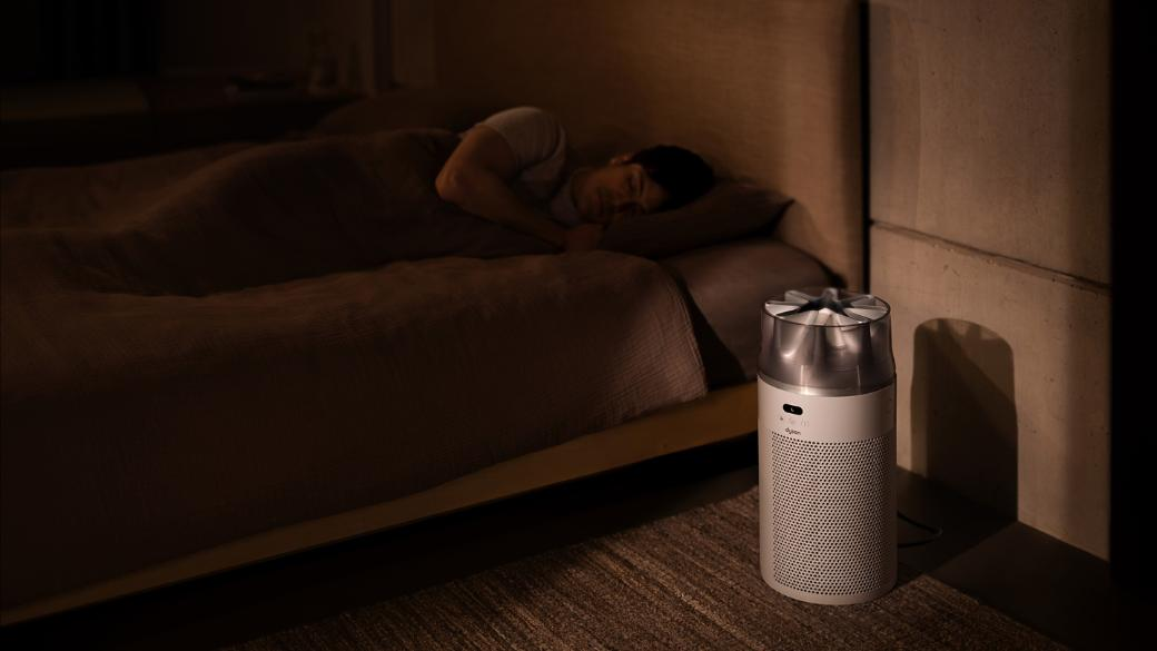 Un homme dort dans un lit, avec un purificateur d'air blanc à côté.
