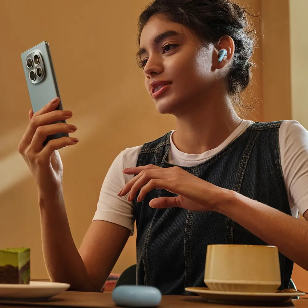 Femme avec écouteurs tient téléphone, assise à table avec gâteau et café.
