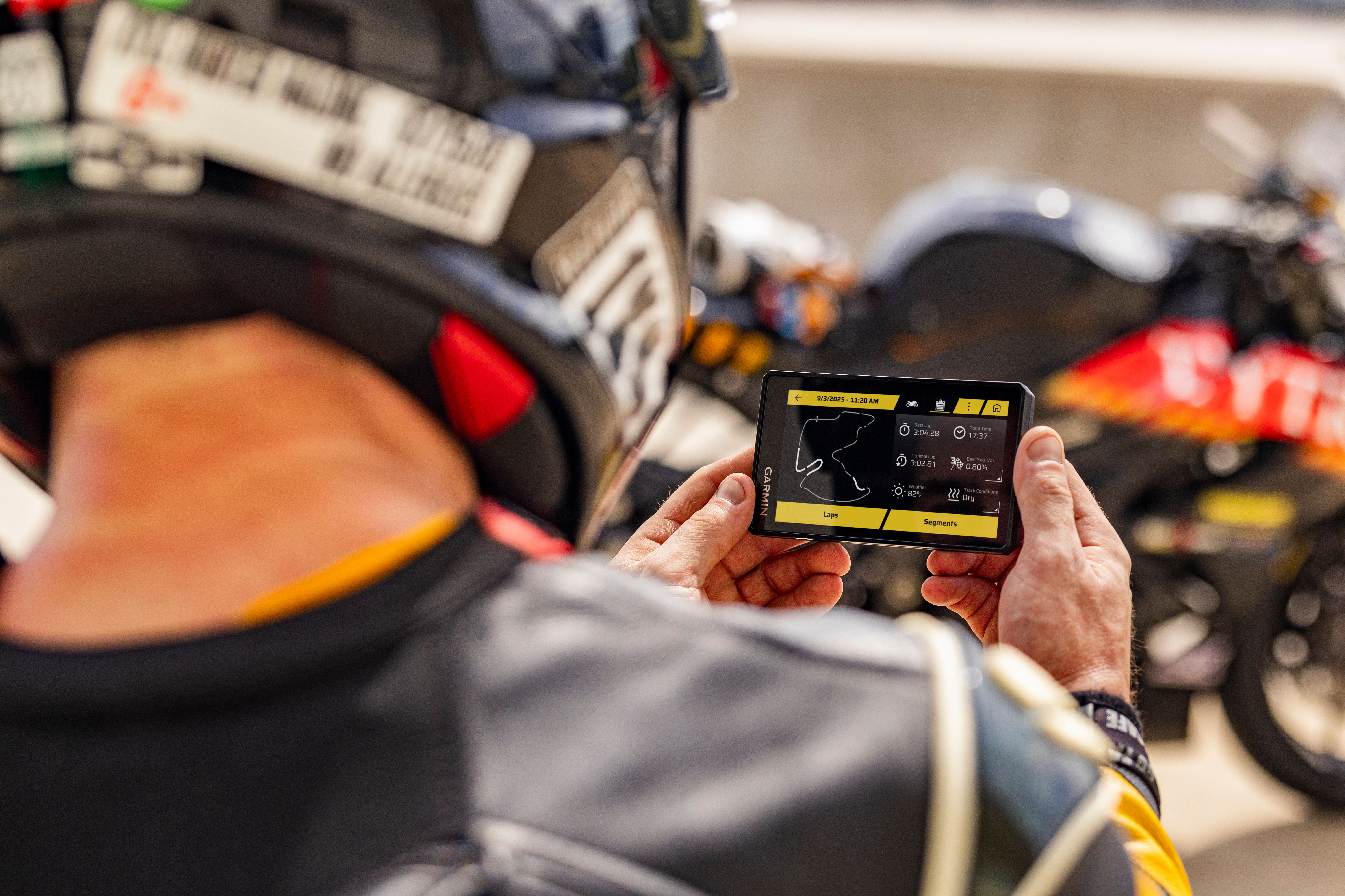 Motorradfahrer hält Smartphone mit Strecken-App, Motorrad im Hintergrund.
