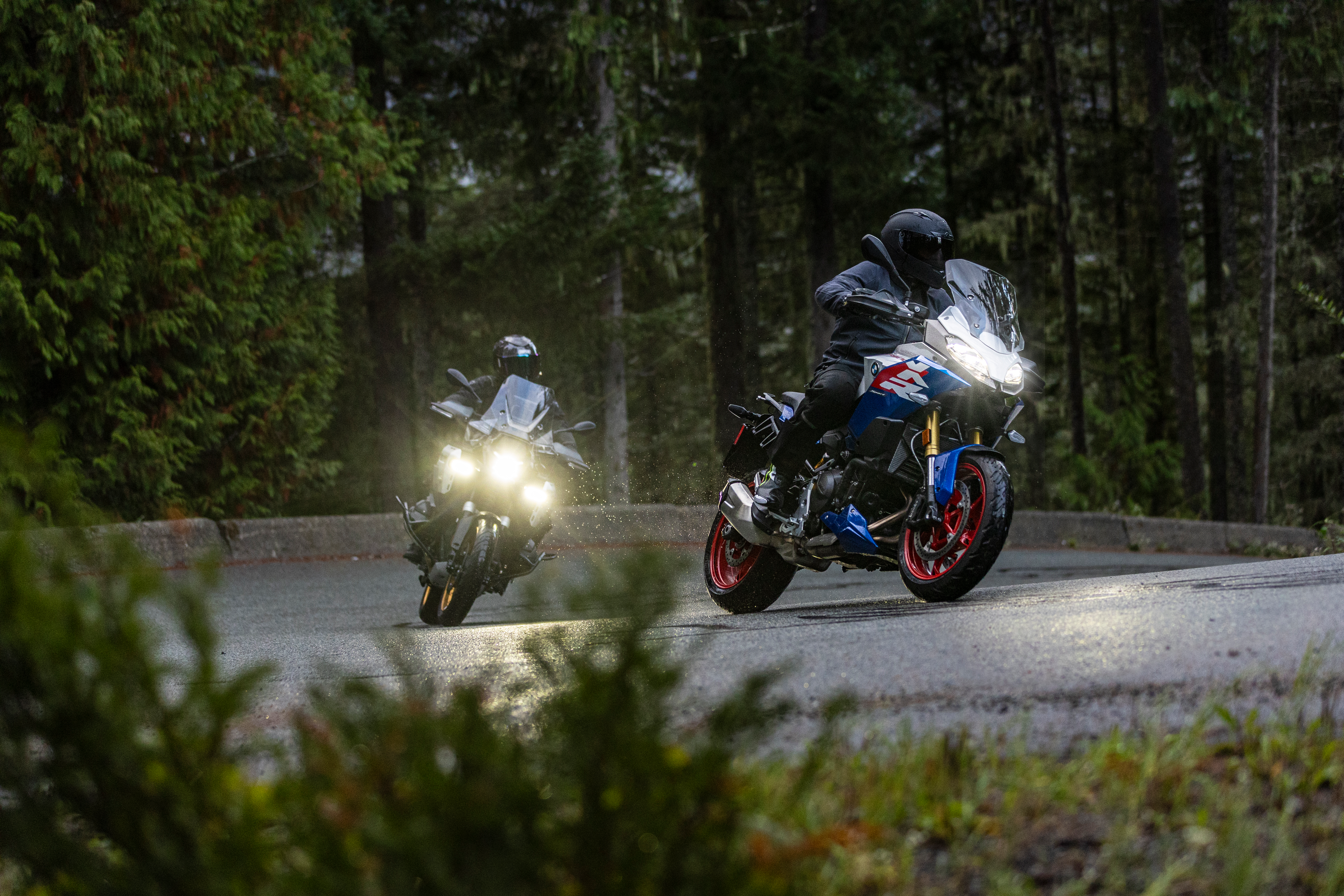 Zwei Motorradfahrer fahren auf einer nassen Straße im Wald.