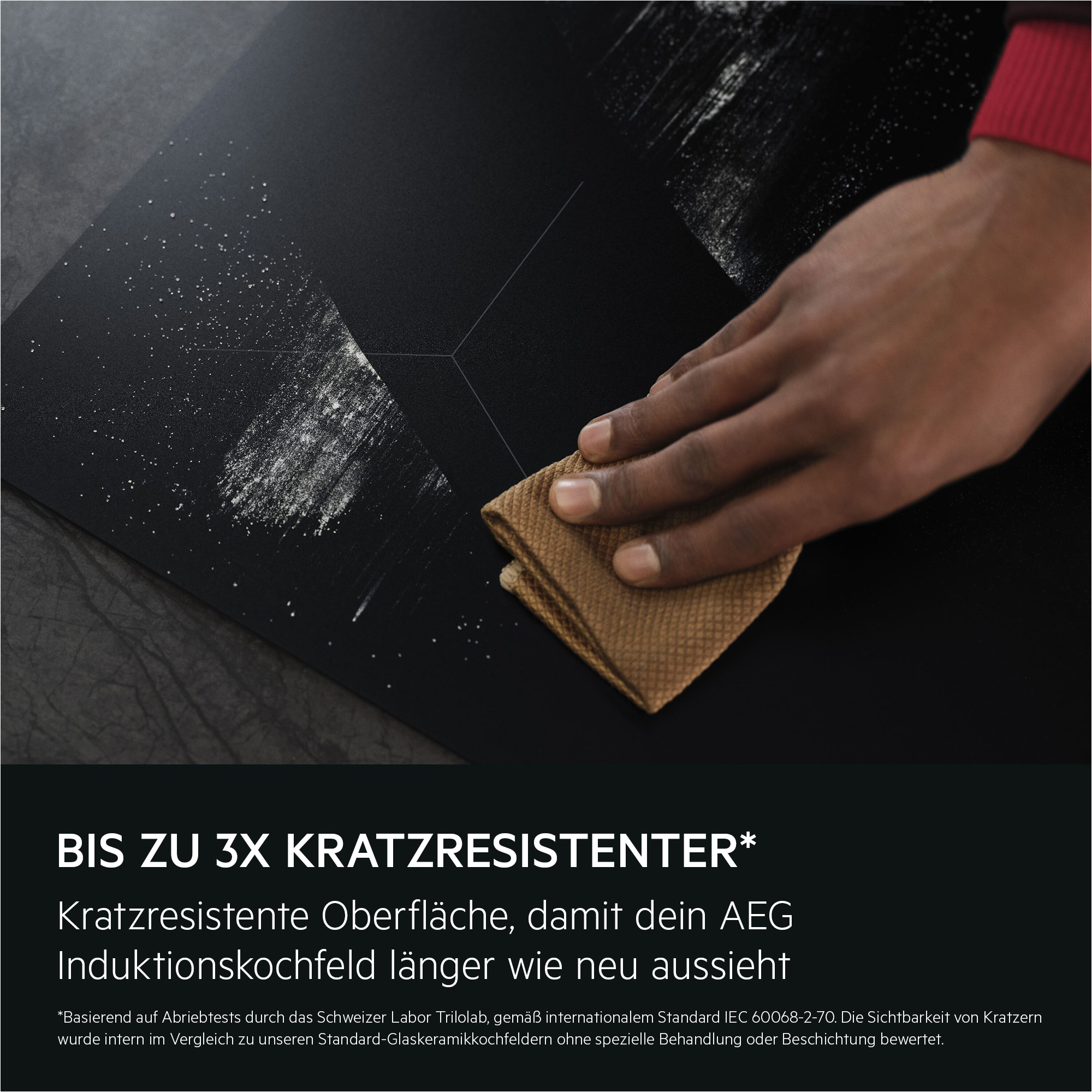 Eine Hand reinigt eine schwarze Kochfläche mit einem braunen Tuch.