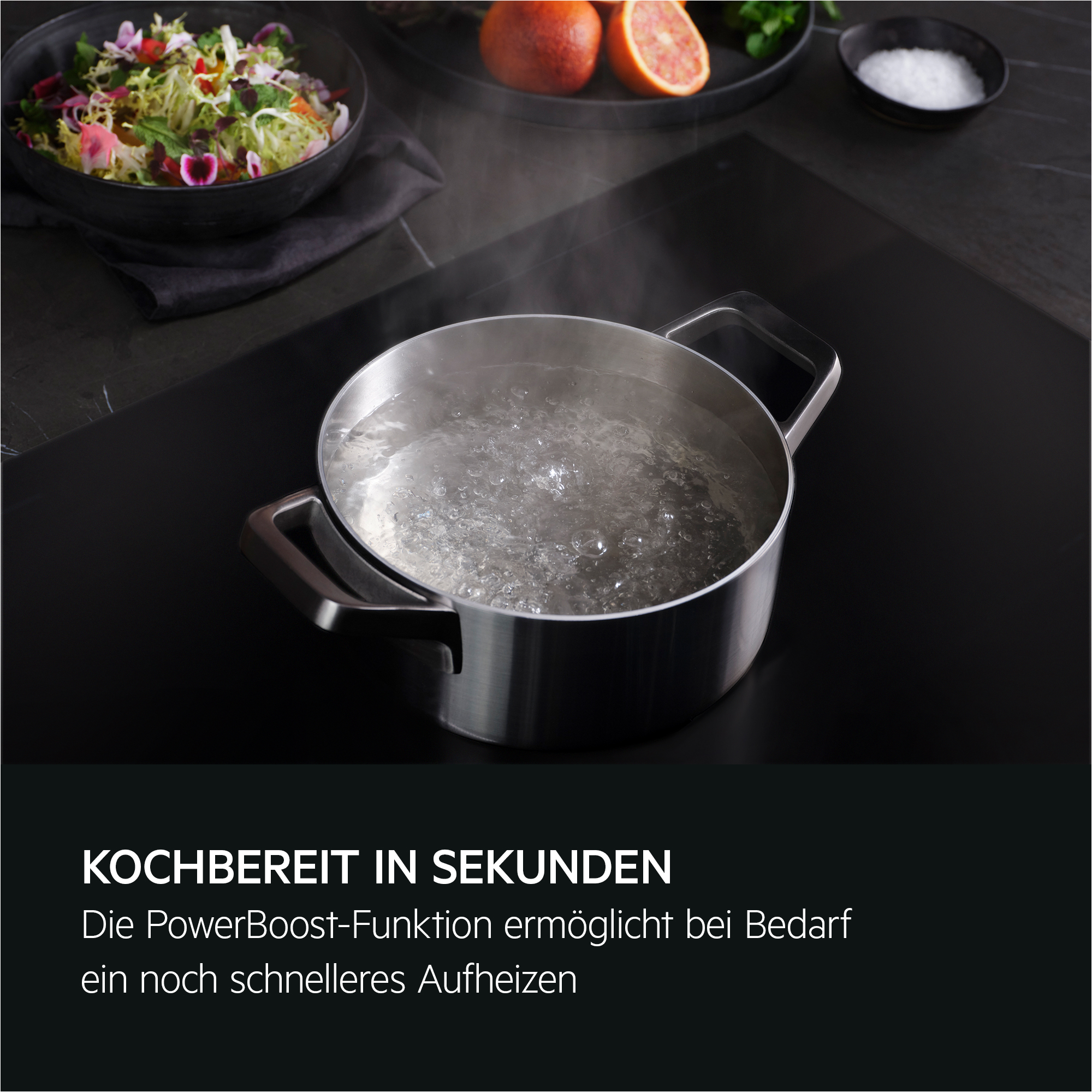 Topf mit kochendem Wasser auf schwarzer Kochfläche, daneben Salat und Orangen.
