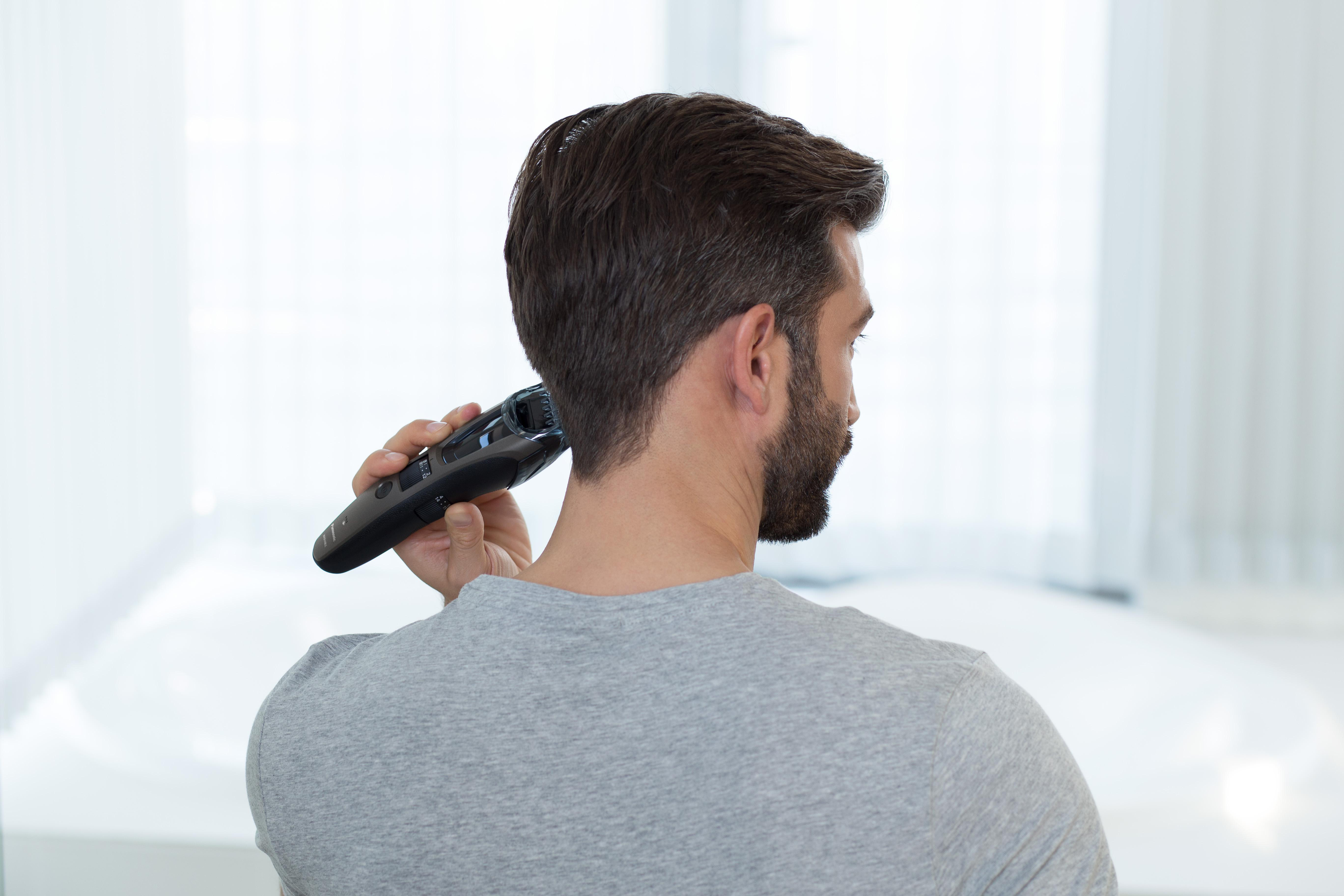 Mann mit Bart trimmt seinen Nacken mit einem schwarzen Trimmer.