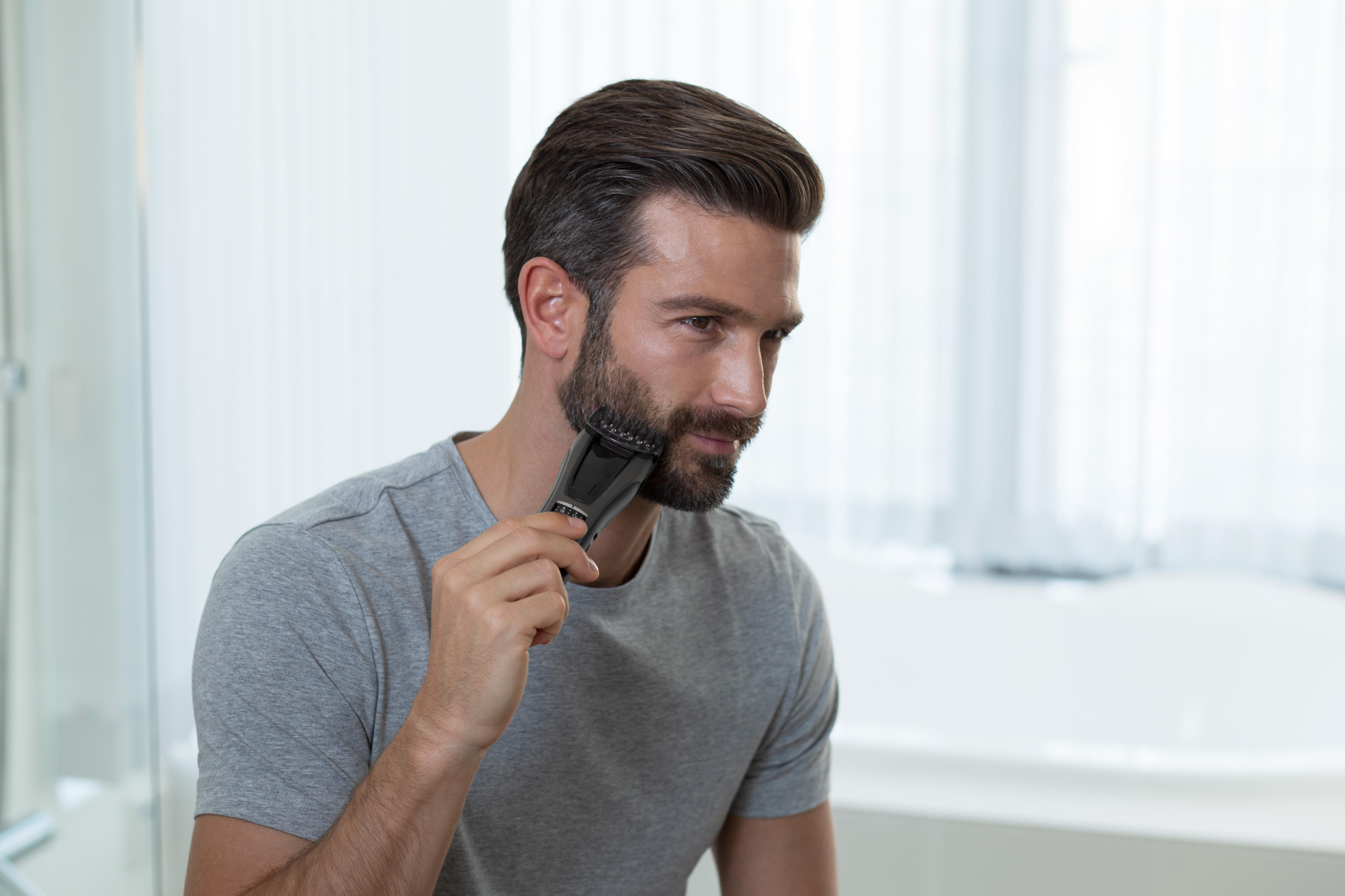 Ein Mann mit Bart trimmt sich den Bart mit einem Trimmer.