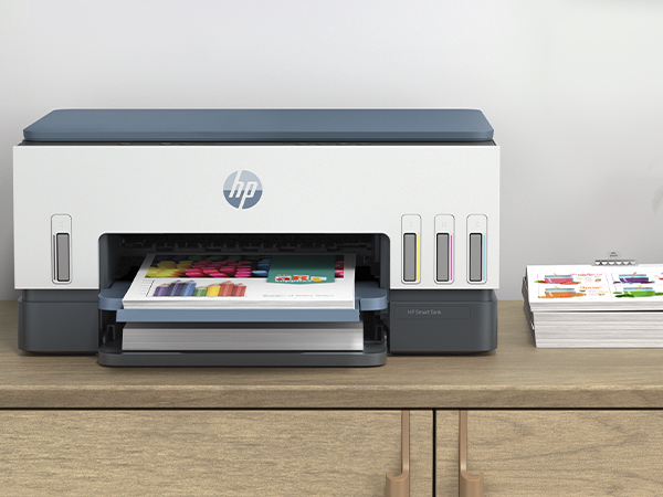 Drukarka HP ze zbiornikami na tusz i papierem na drewnianym biurku.