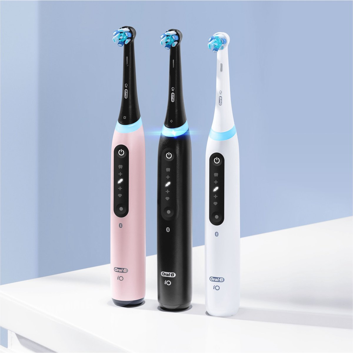 Three electric toothbrushes: pink, black, and white, with blue bristles.