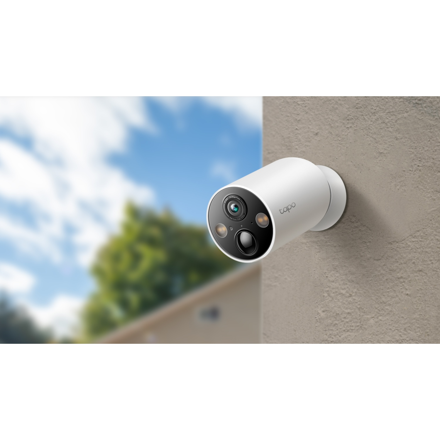 A white Tapo security camera is mounted on a textured wall. Trees and sky are blurred in the background.