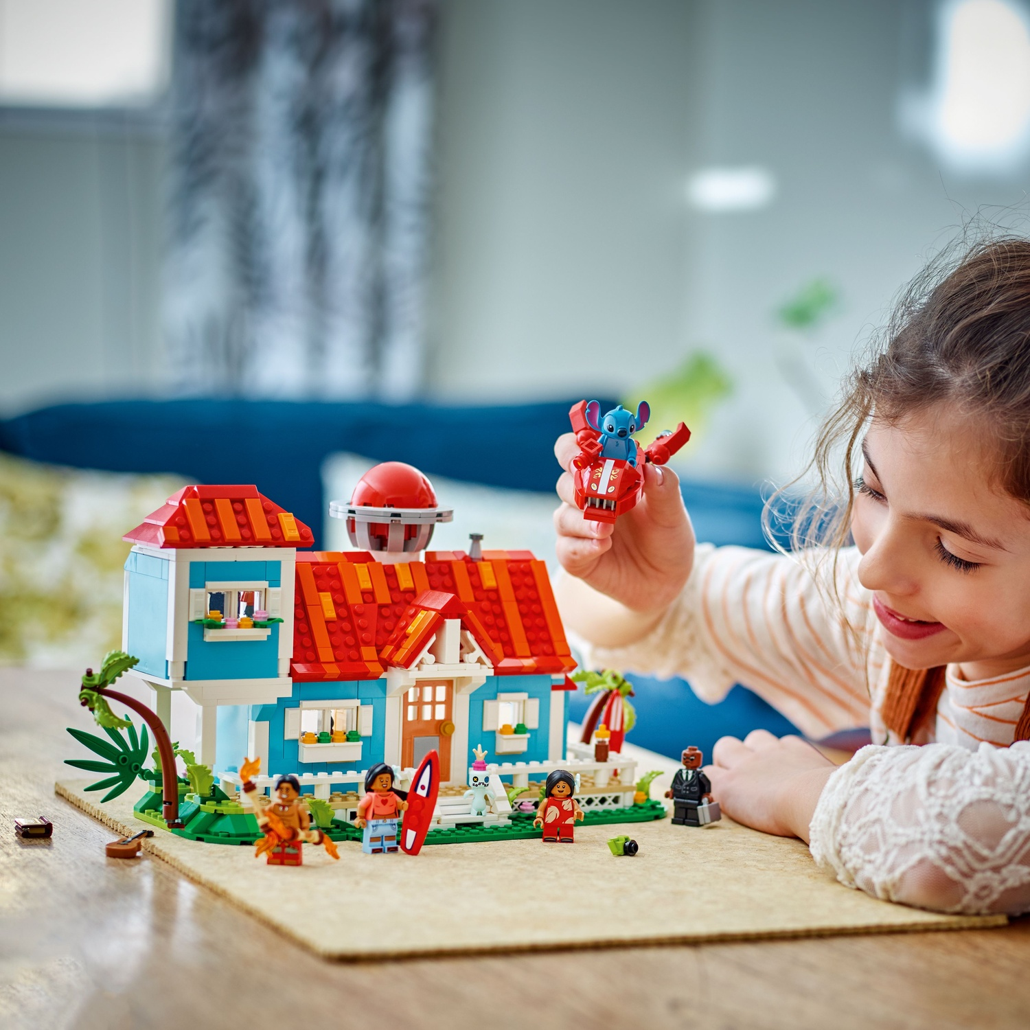Une fille joue avec une maison Lego colorée et des figurines, dont Stitch.