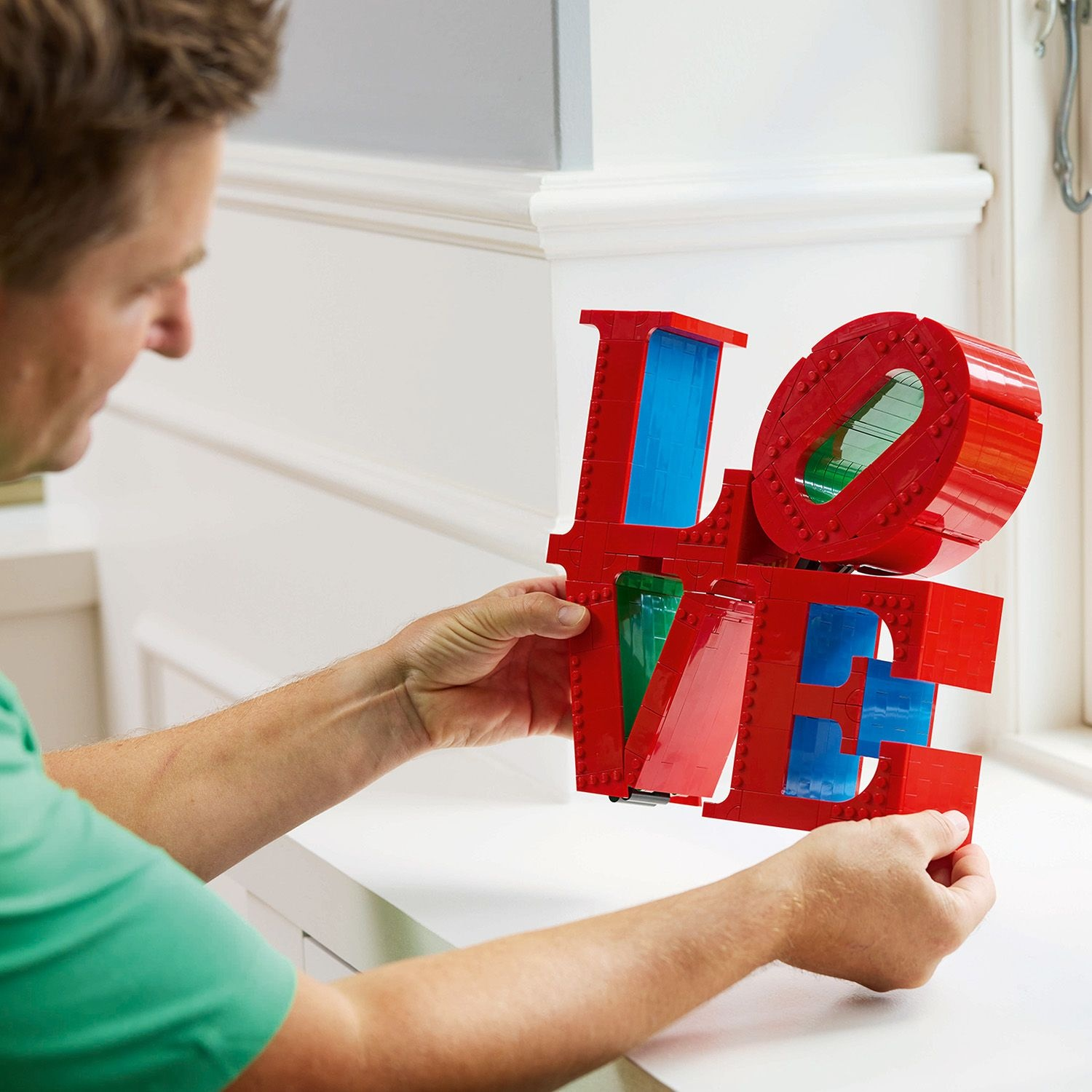 Man holds red Lego letters spelling LOVE, with blue and green accents.