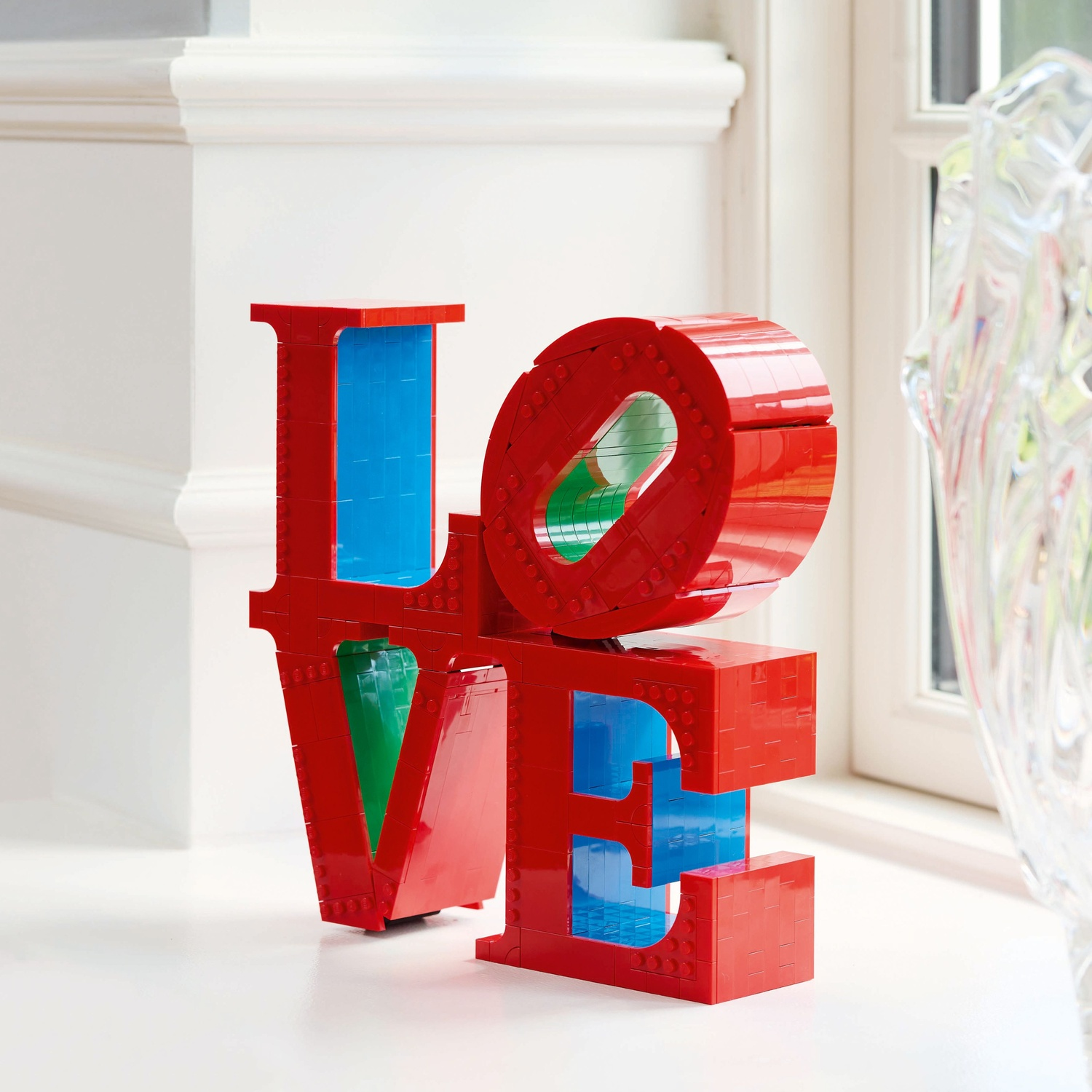 Red LEGO word LOVE with blue and green accents on a white table.