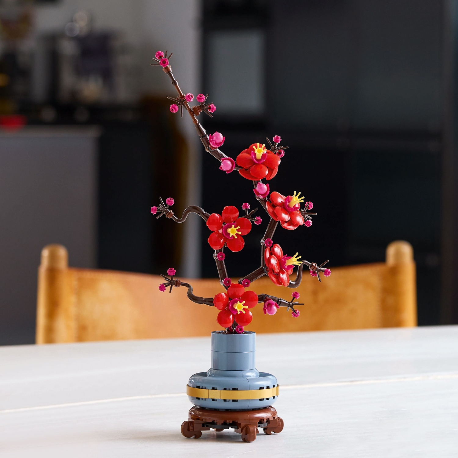 Een Lego-model van een bloeiende kersenboomtak in een blauwe vaas op een tafel.