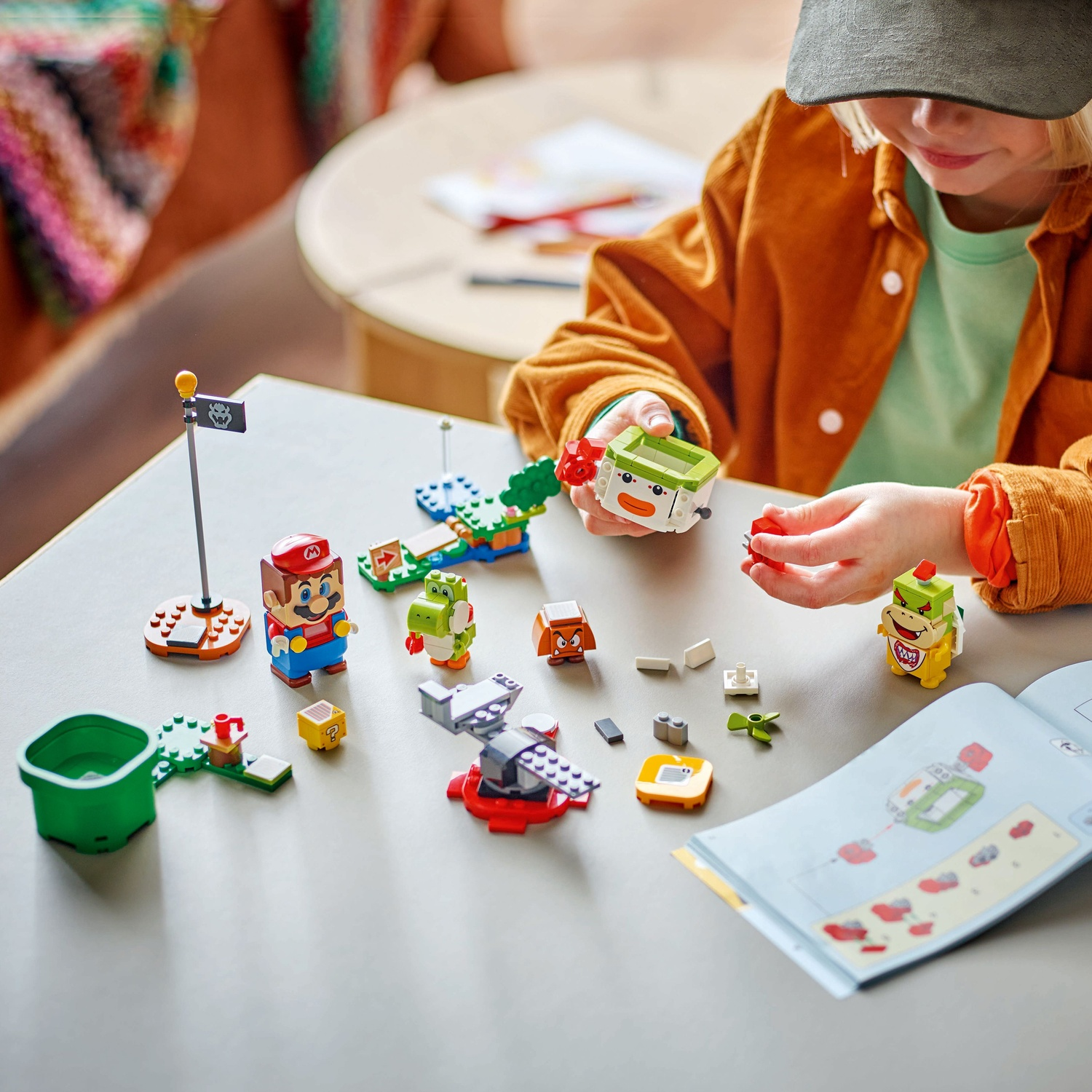 Child building Lego Mario figures. Mario, Yoshi, and Bowser are visible.