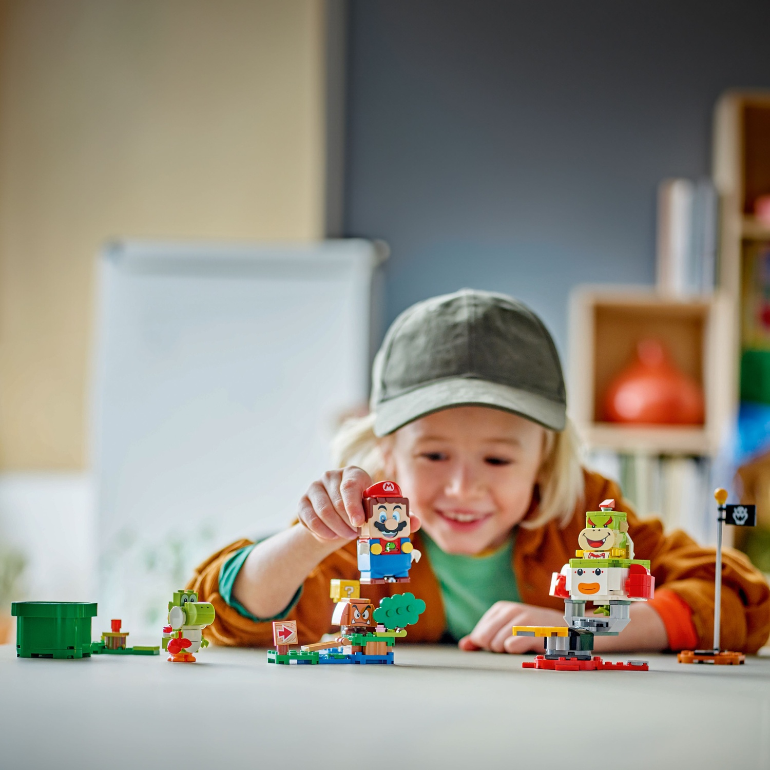 A child plays with Lego figures of Mario, Yoshi, and Bowser on a table.