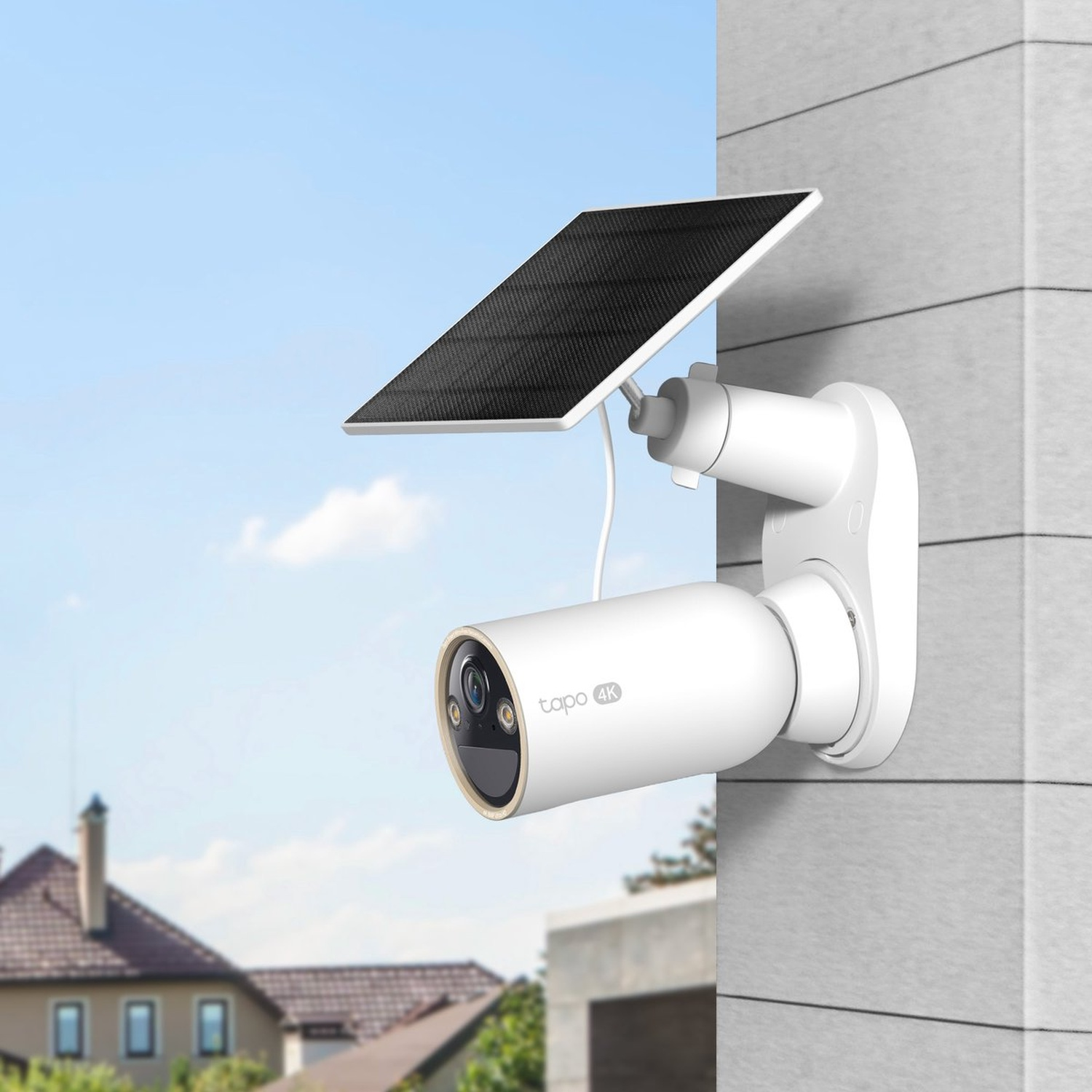 White security camera with solar panel mounted on house wall, blue sky.