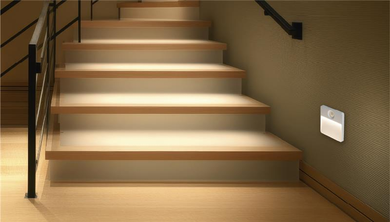 Verlichte houten trap met metalen leuning en wandlamp.