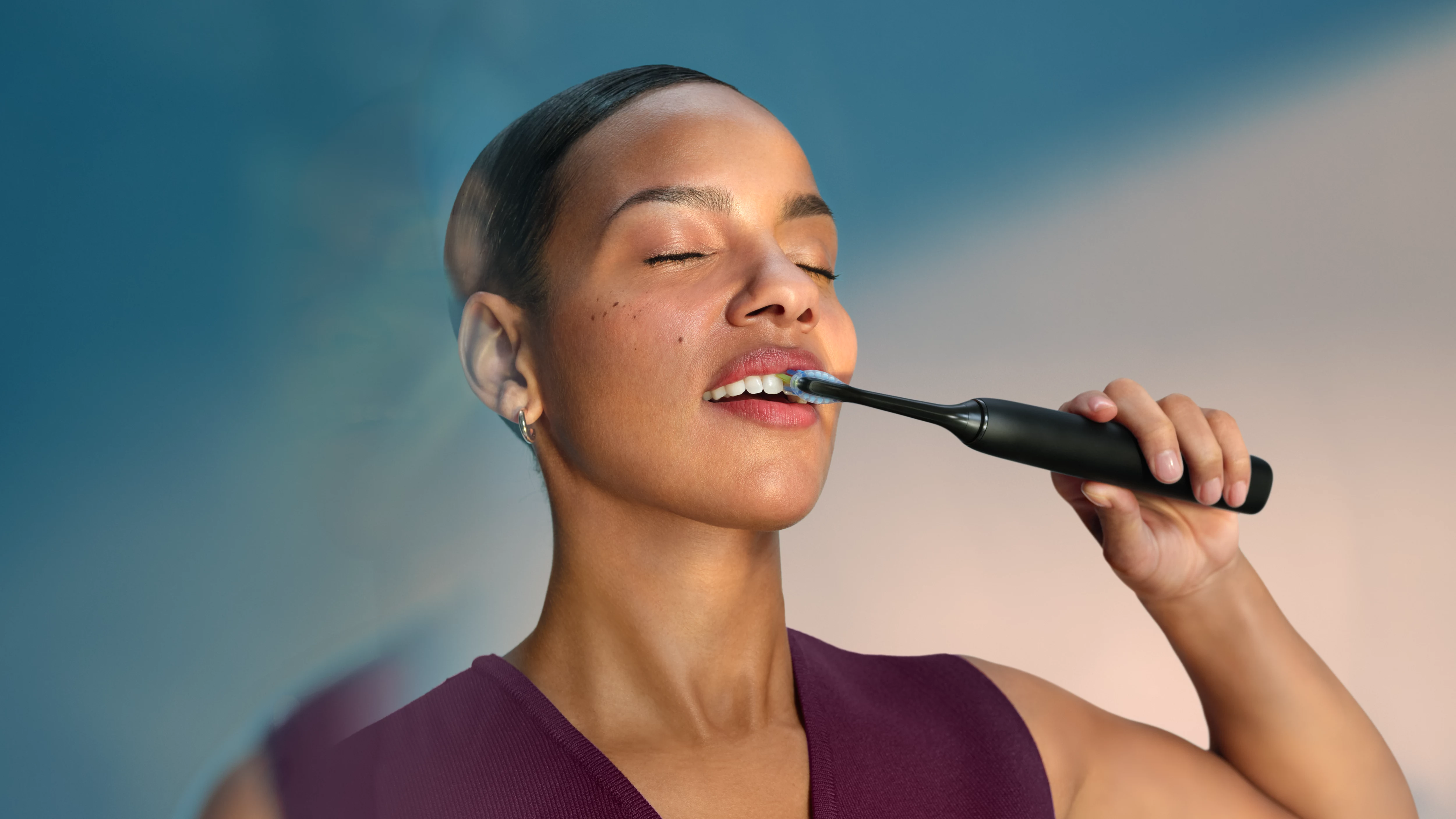 Kobieta z zamkniętymi oczami myje zęby czarną szczoteczką elektryczną.