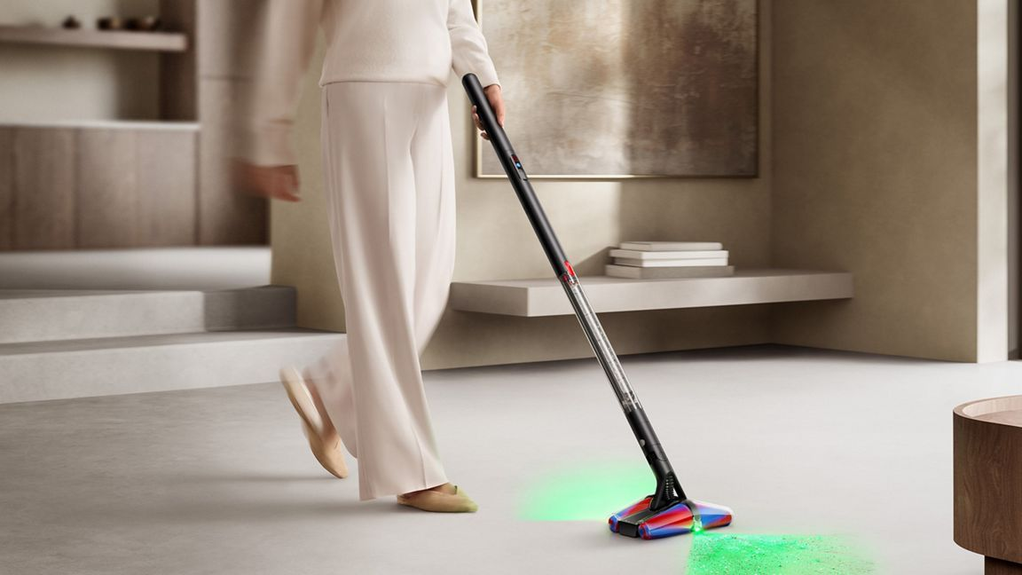 Personne passant l'aspirateur avec un appareil éclairé sur sol clair.