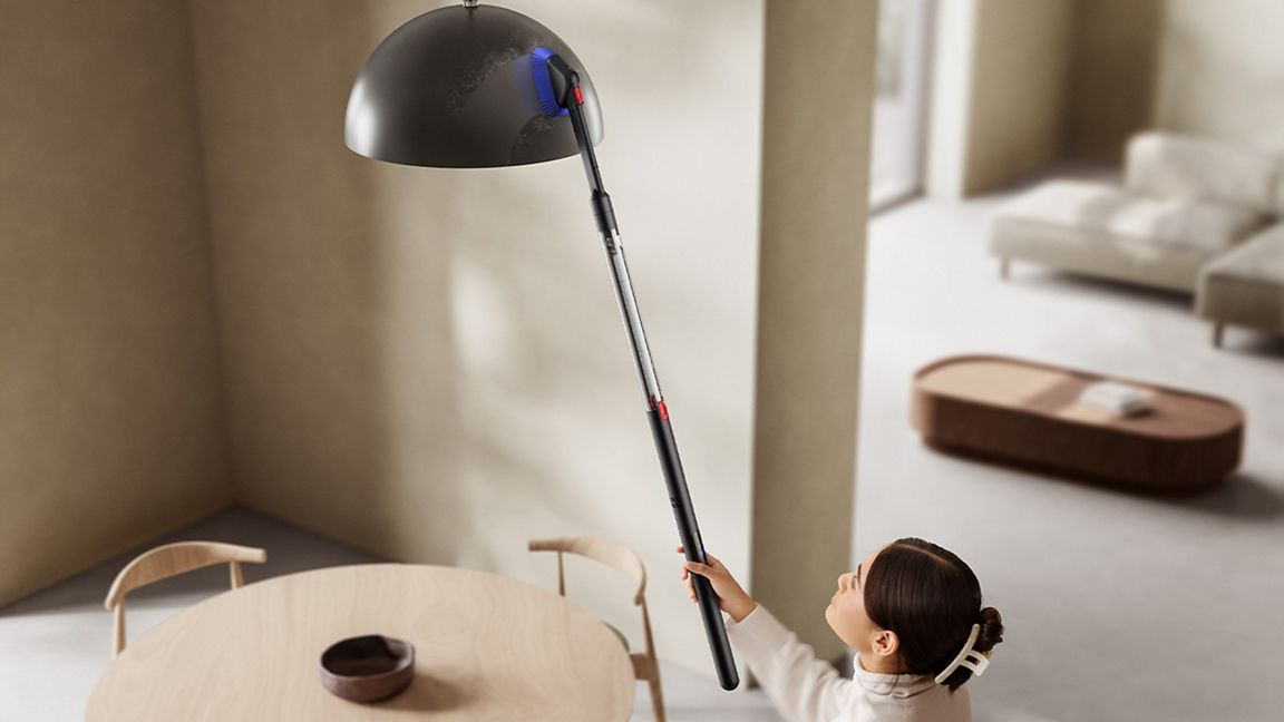 Une femme nettoie une lampe avec un accessoire d'aspirateur dans une salle à manger moderne.