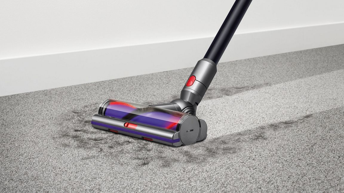 Une tête d'aspirateur nettoie un tapis gris, avec des traces de saleté visibles.