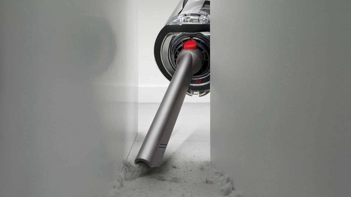 Un aspirateur aspire la poussière d'un espace étroit entre les murs.