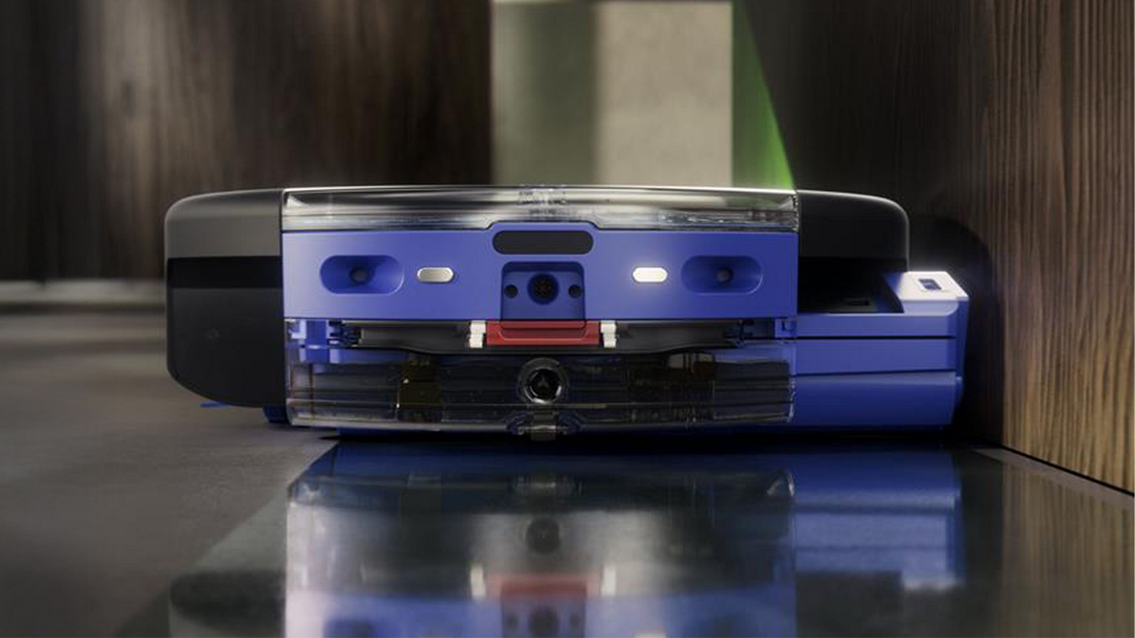 Un aspirateur robot bleu avec des détails transparents se déplace sur un sol sombre.
