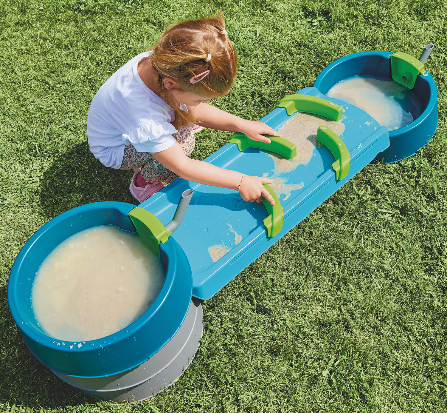 Ein kleines Mädchen spielt mit einem blauen und grünen Wasserspieltisch im Gras.
