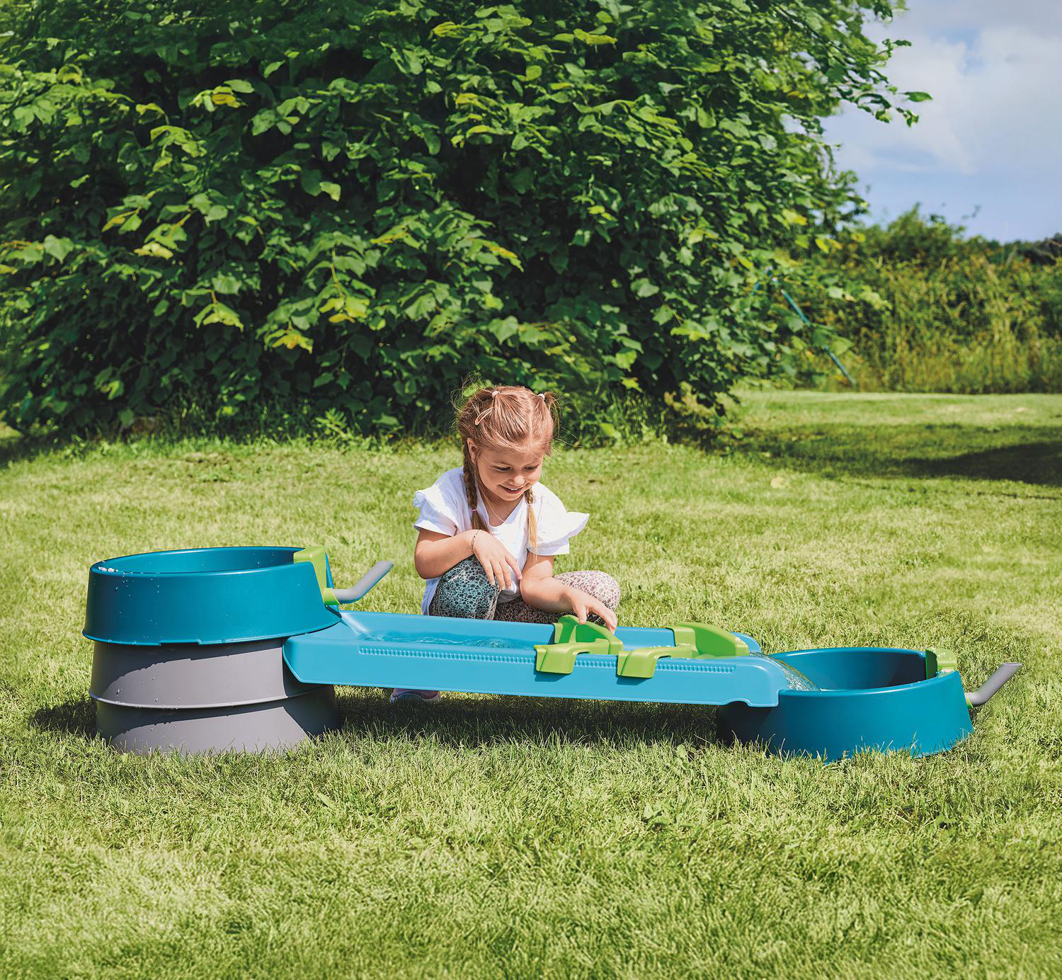 Ein kleines Mädchen spielt mit einem Wasserspielzeug im Garten auf dem Rasen.