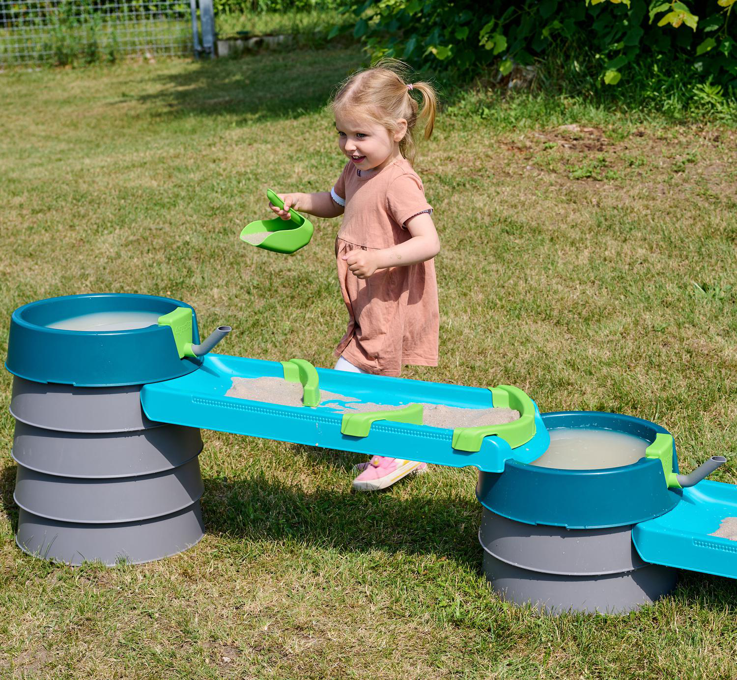 Ein kleines Mädchen spielt mit einem Sand- und Wasserspielzeug im Garten.