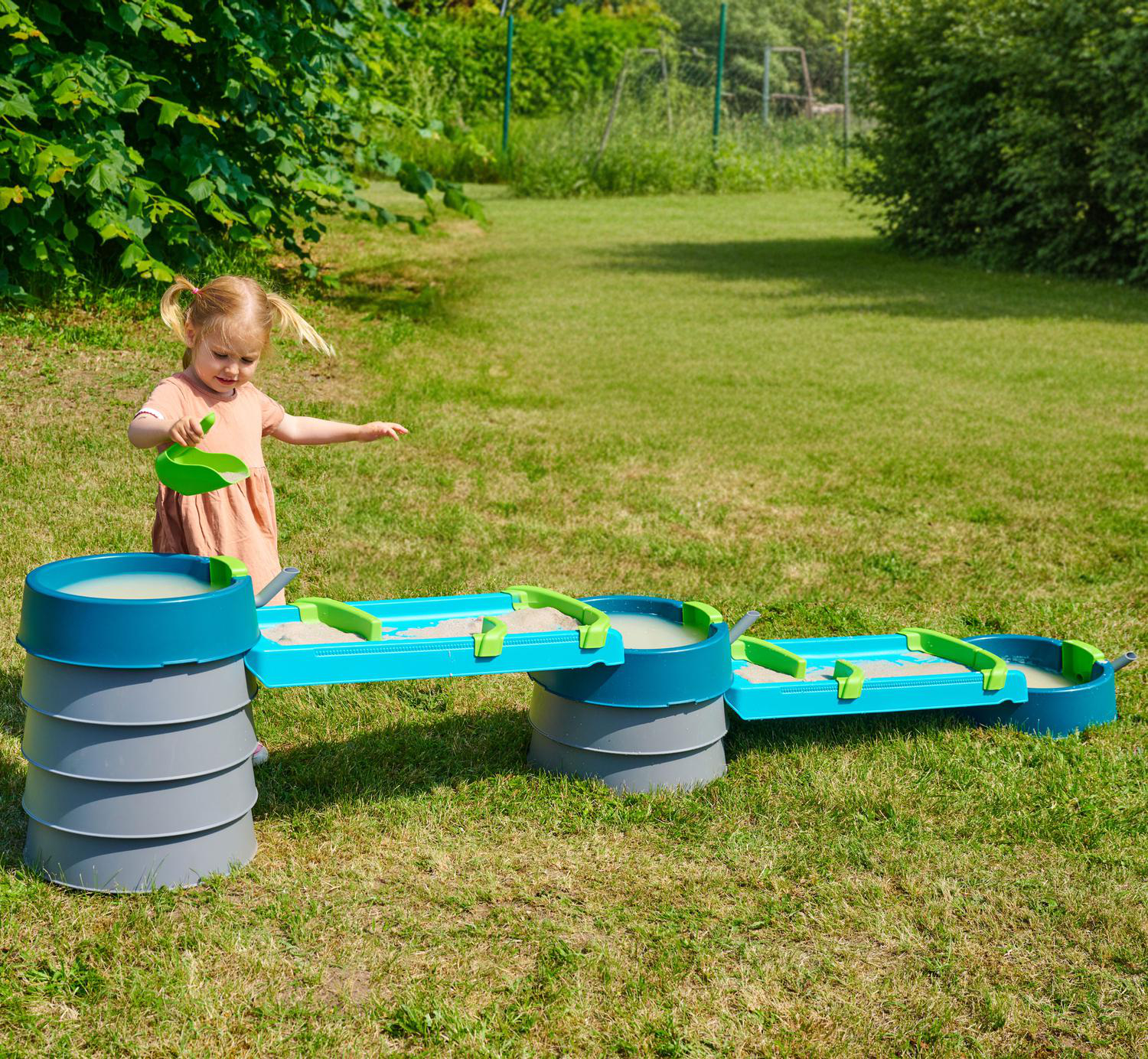 Ein kleines Mädchen spielt mit einem Wasserspieltisch im Garten.