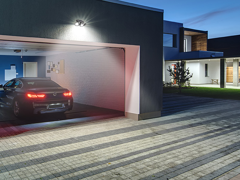 Ciemny samochód cofa do garażu, oświetlony przez lampę.