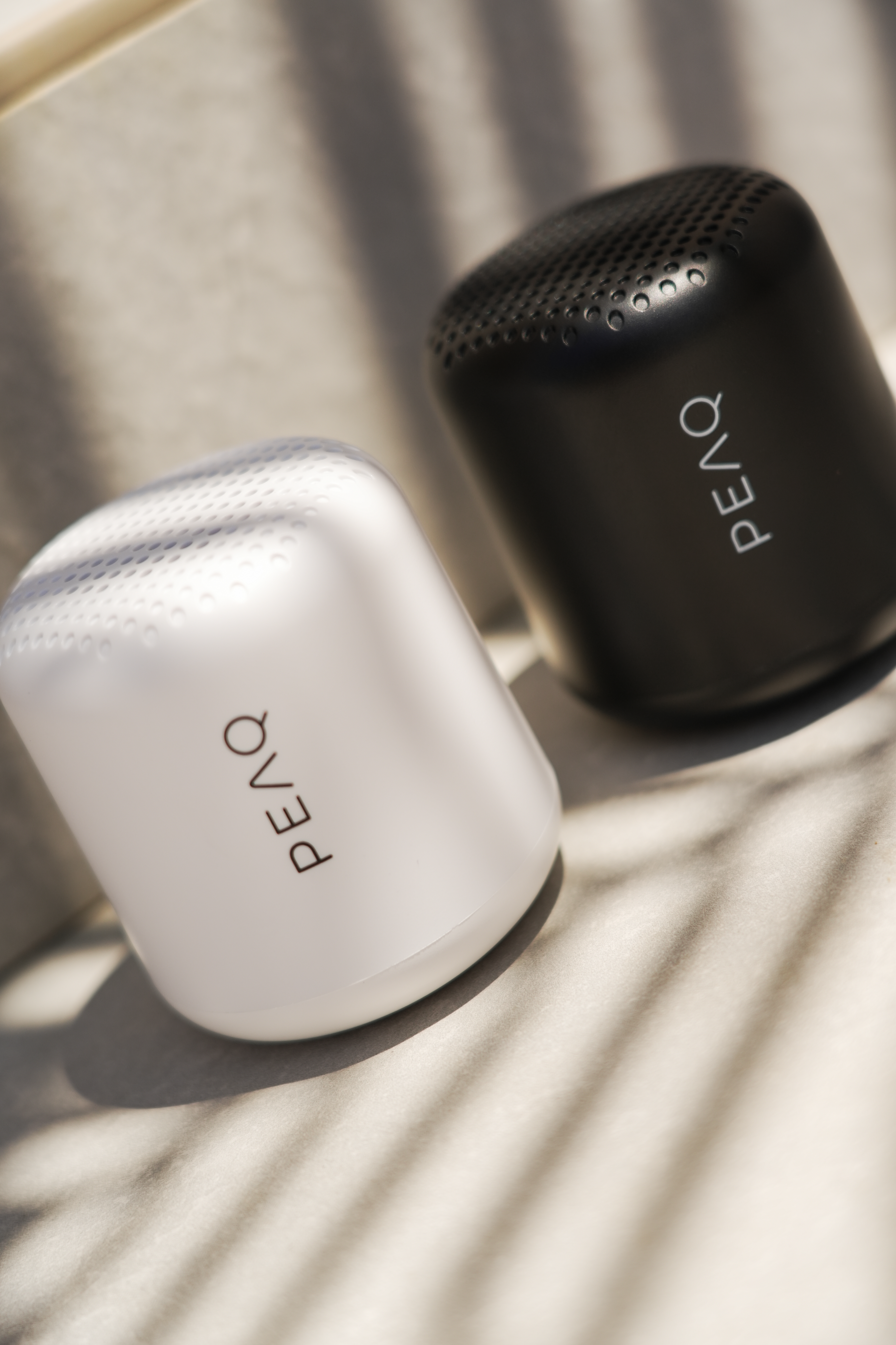 Dwa głośniki PEAQ, czarny i biały, na jasnej powierzchni z cieniami.