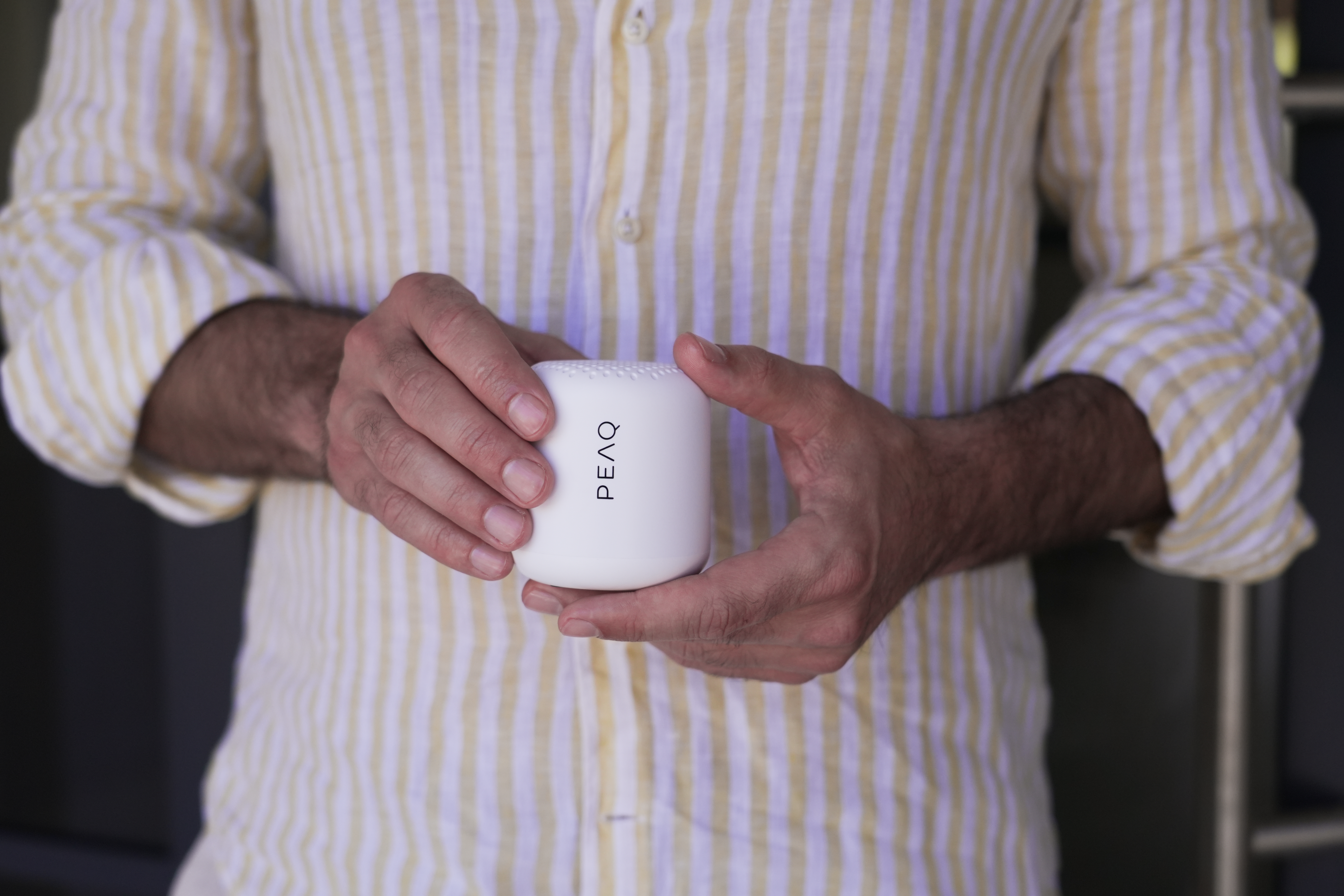 Mężczyzna trzyma białe pudełko PEAQ z otworami, nosi koszulę w paski.