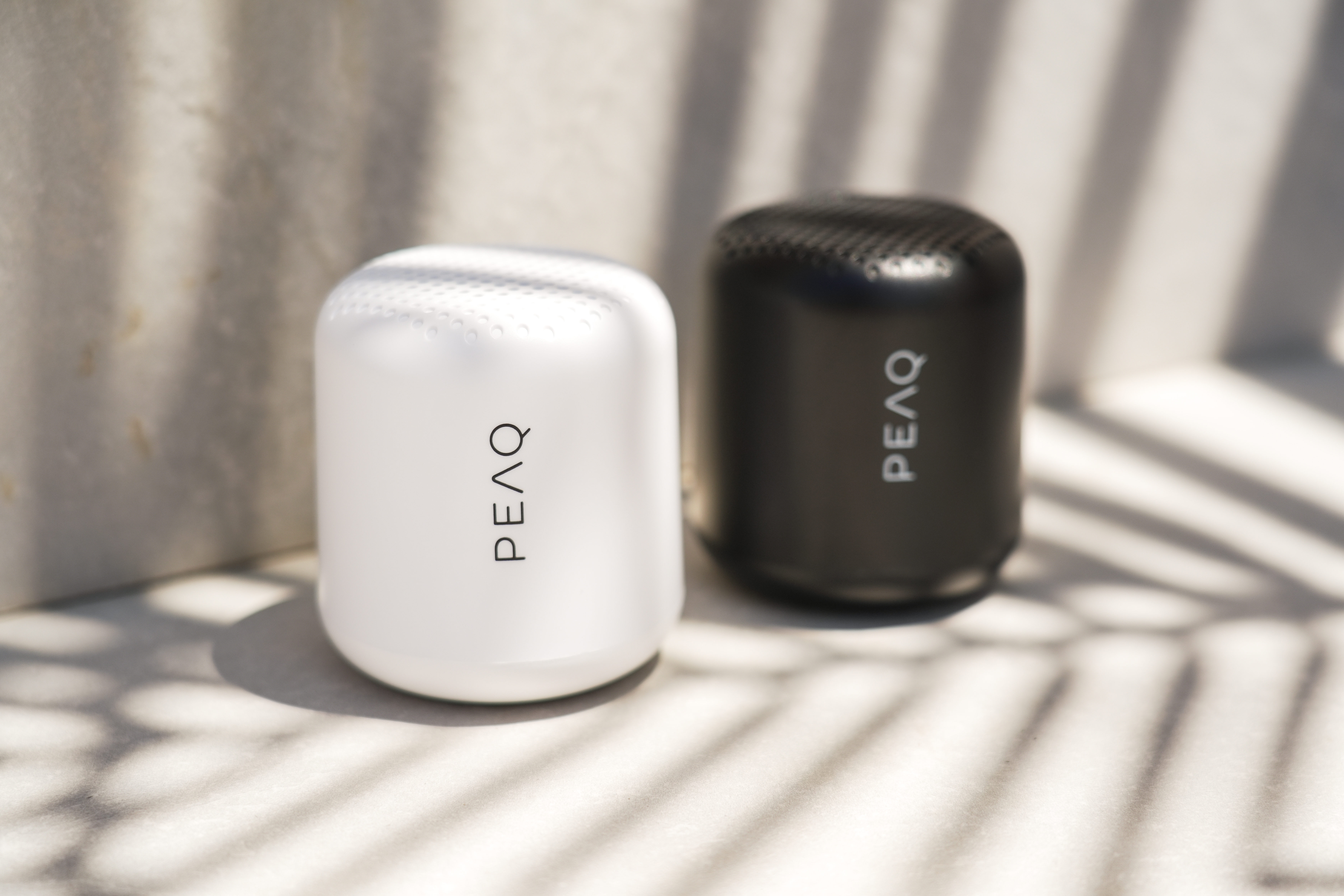 Dwa głośniki PEAQ, jeden biały, jeden czarny, stoją obok siebie.