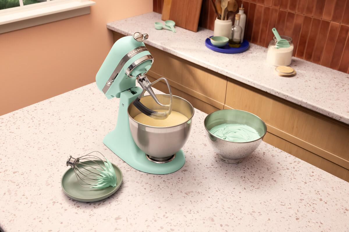 Ein türkisfarbener Küchenmixer mit Rührschüssel und Teig. Daneben eine Schüssel mit blauer Creme.