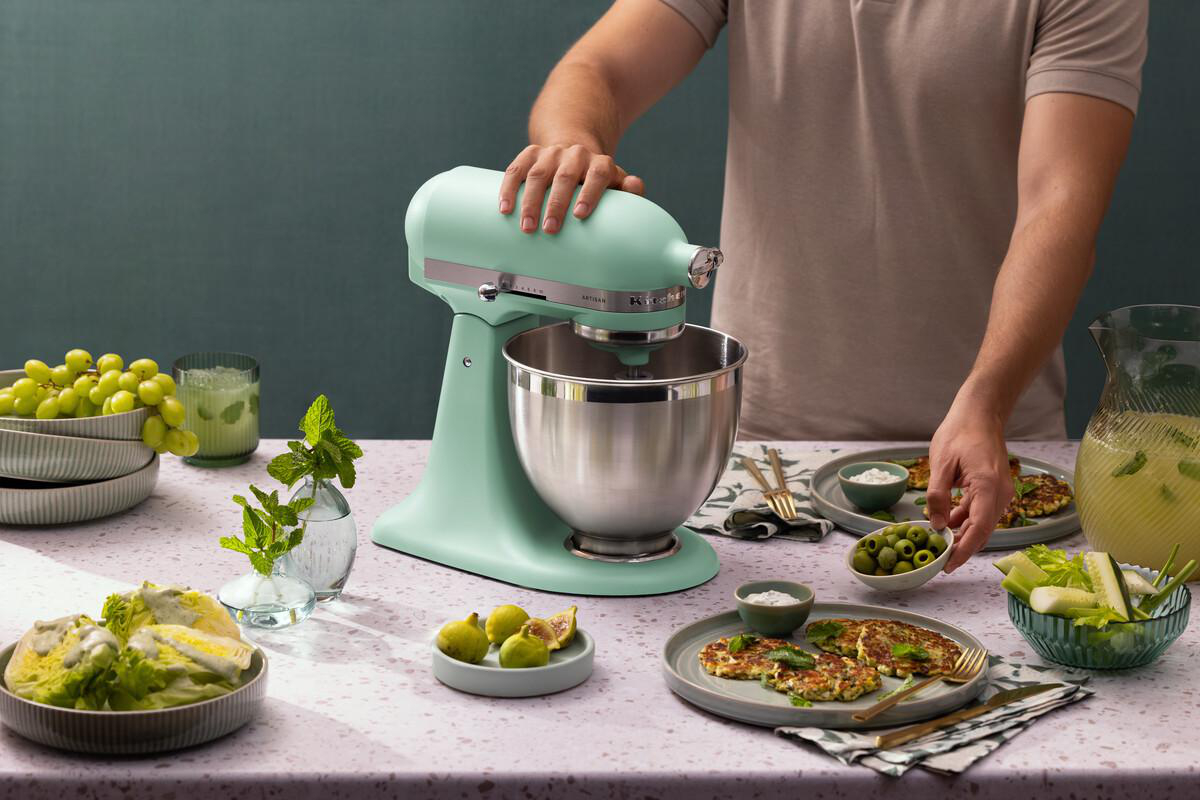 Ein mintgrüner Küchenmixer steht auf einem Tisch mit Lebensmitteln.