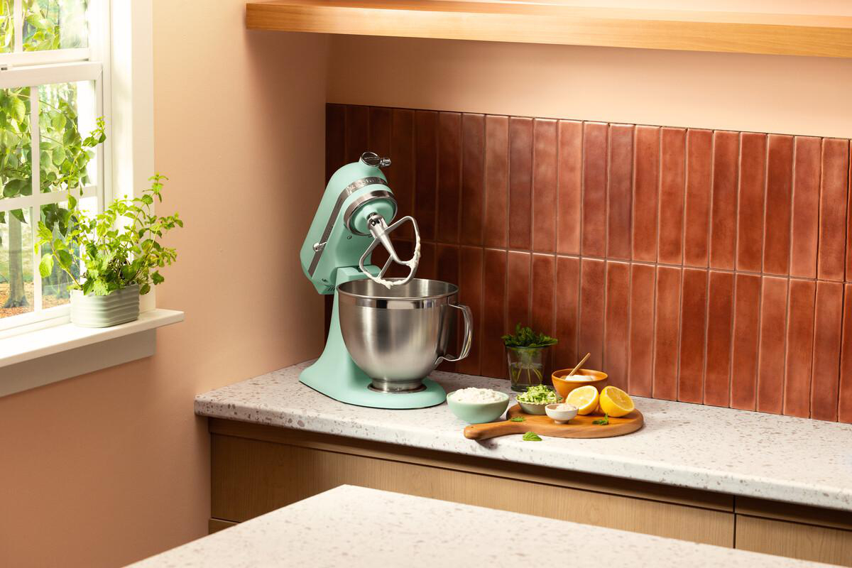 Ein mintgrüner Küchenmixer steht auf einer Arbeitsplatte neben Schalen mit Zutaten.
