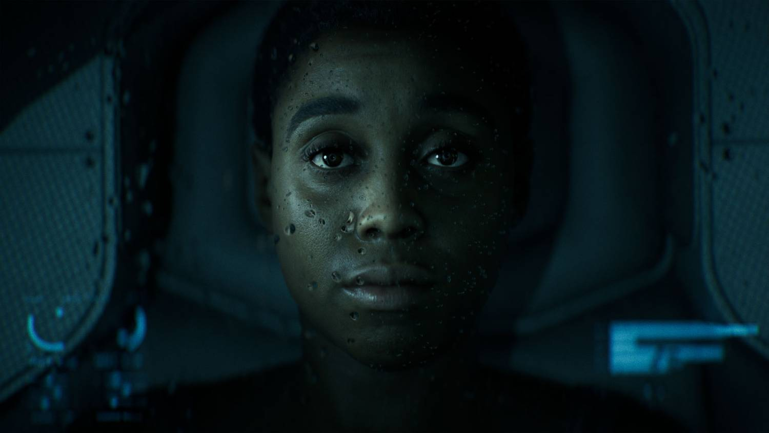 Primer plano de un rostro joven con gotas de agua en la piel, fondo oscuro.