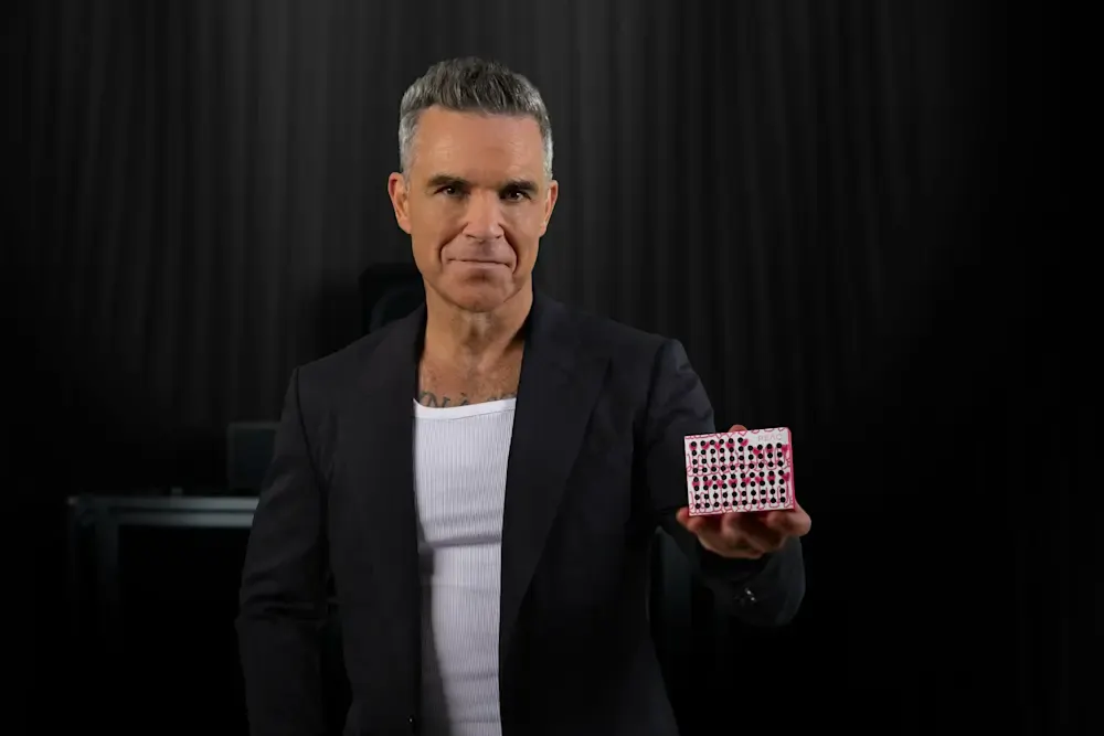 Mężczyzna z siwymi włosami w garniturze trzyma małe białe pudełko z czarnymi kropkami.