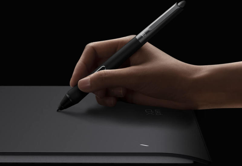 Una mano tiene uno stilo nero su una tavoletta grafica scura.