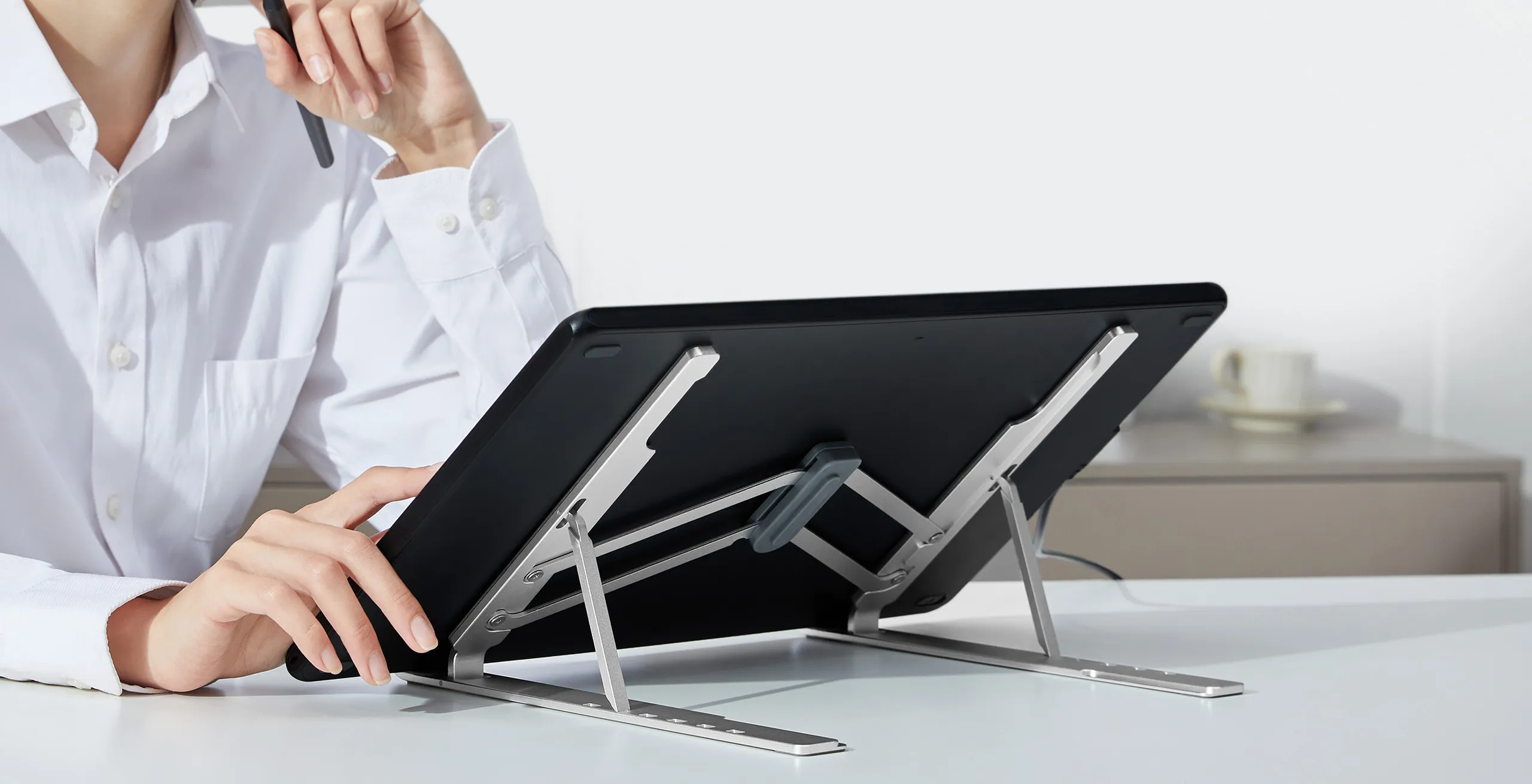 Persona in camicia bianca tiene penna su tablet nero su supporto argentato.