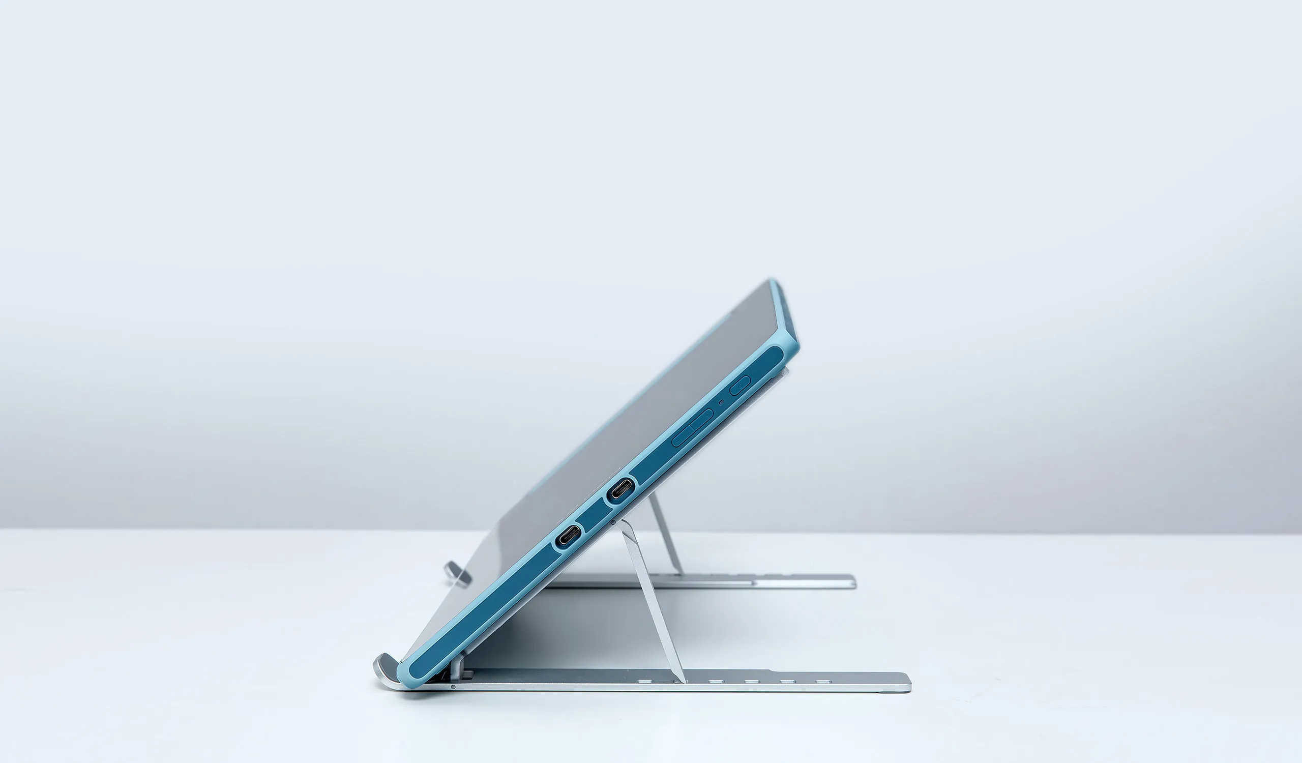 Un tablet blu poggia su un supporto argentato su sfondo bianco.