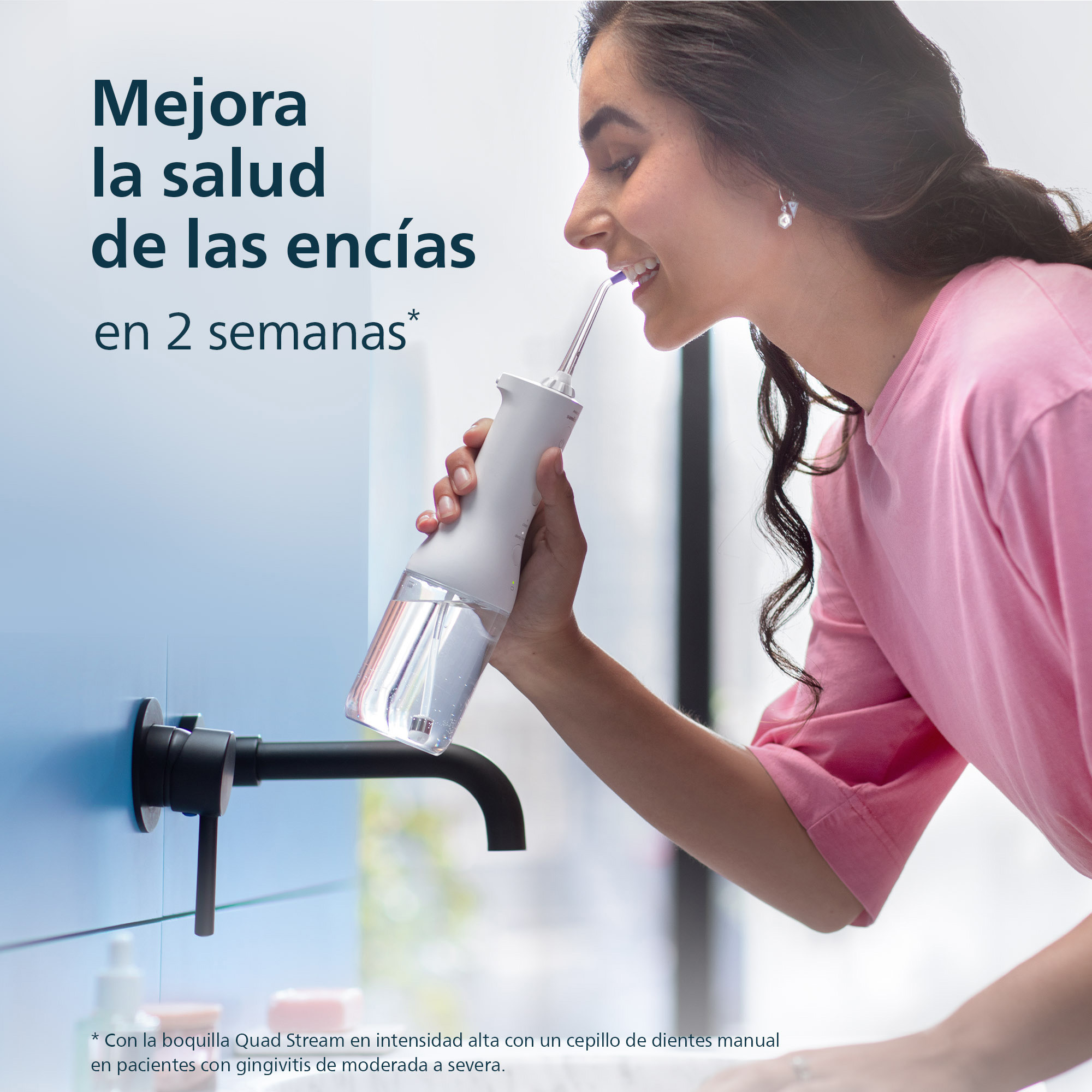 Una mujer usa un irrigador bucal eléctrico. Lleva una camiseta rosa.