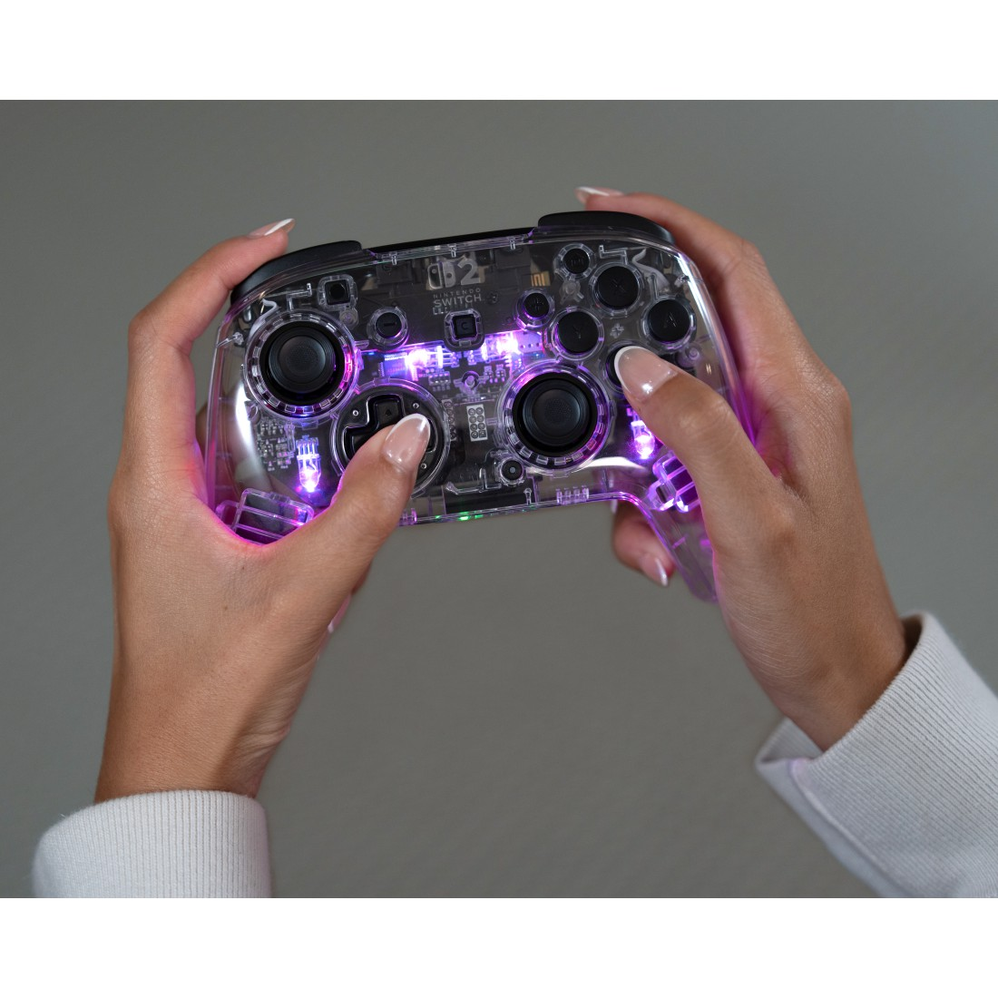 Hände halten einen transparenten Controller mit lila Lichtern.