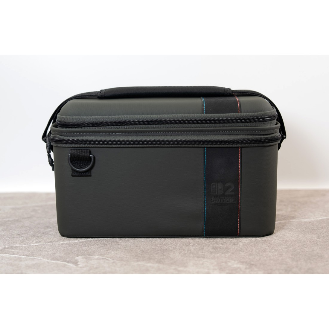 Eine dunkle Nintendo Switch-Tasche mit roten und blauen Nähten steht auf einem Steinboden.