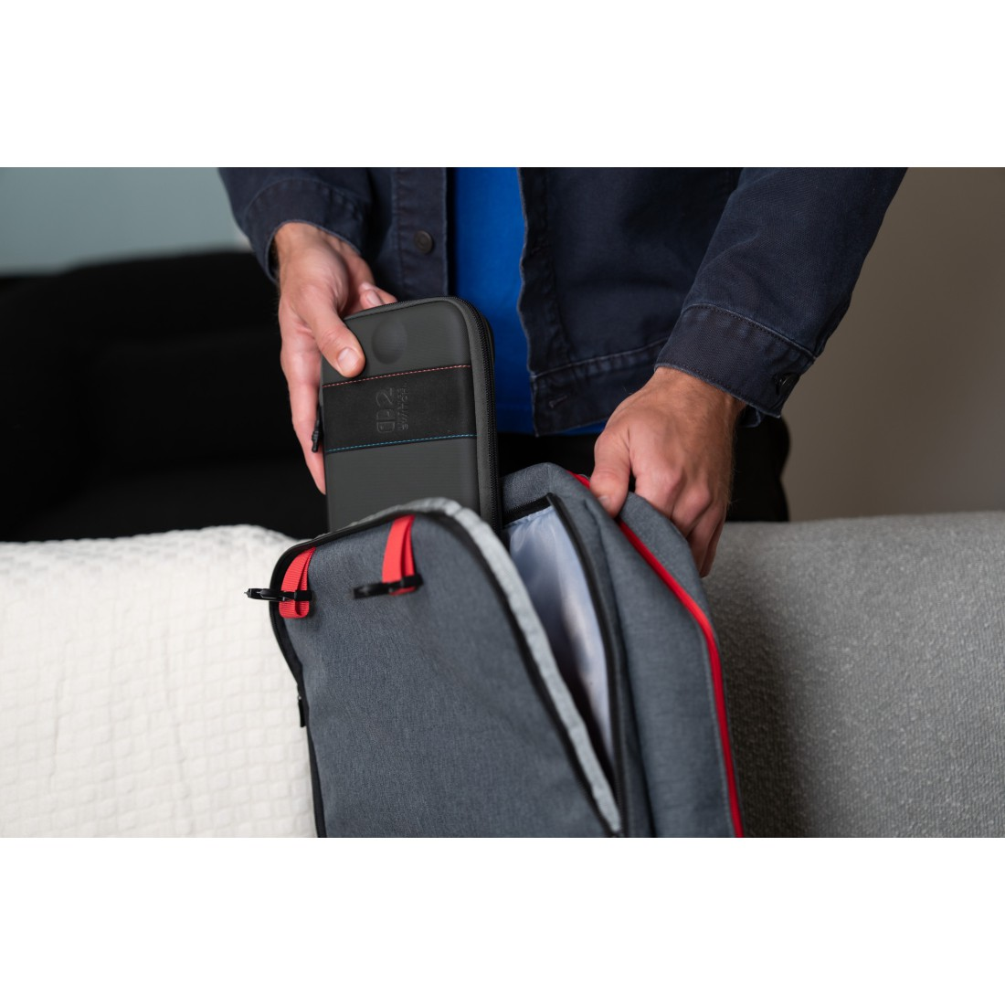 Mann legt graue Hülle mit roten und blauen Akzenten in grauen Rucksack.