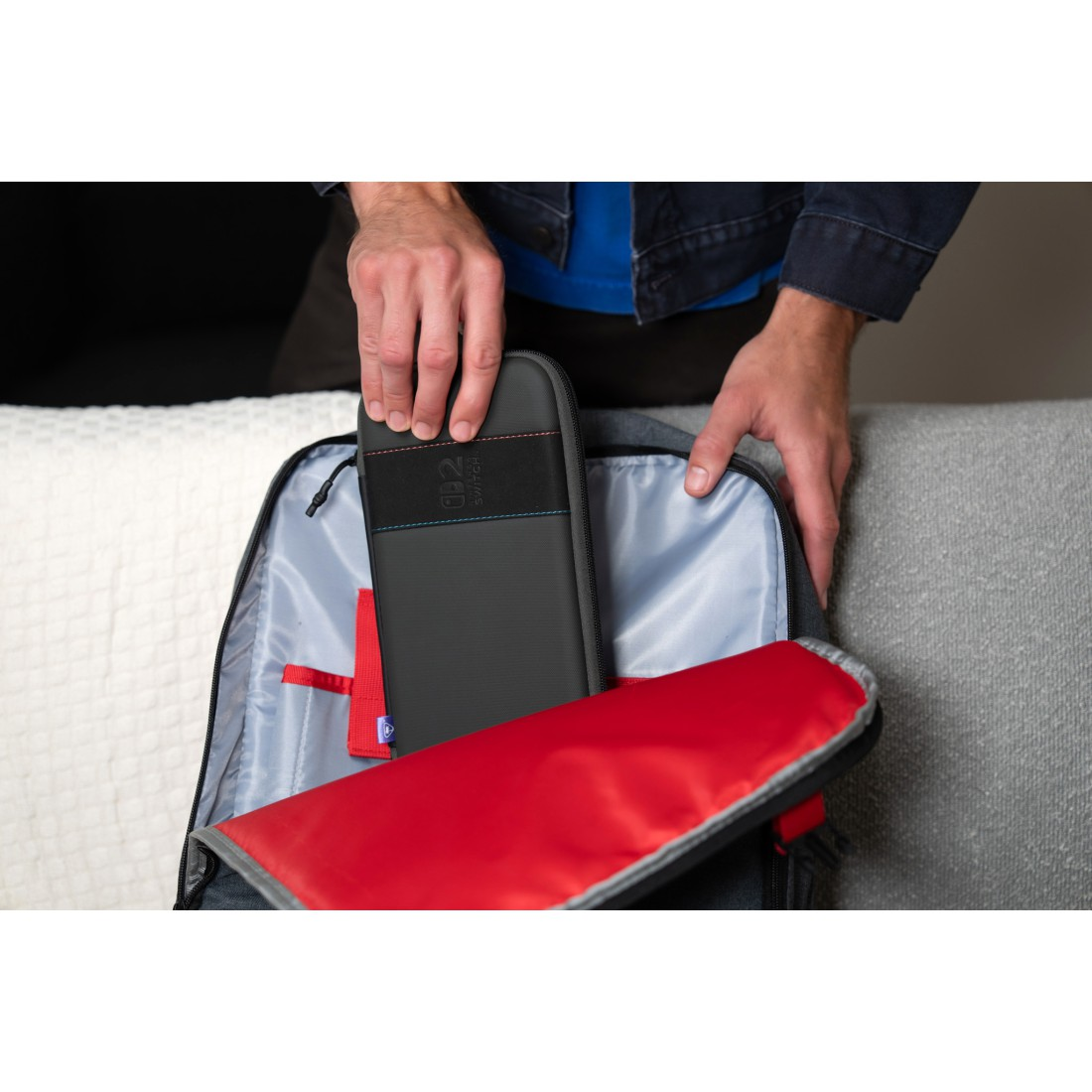 Person legt eine schwarze Nintendo Switch-Hülle in einen Rucksack mit rotem Futter.