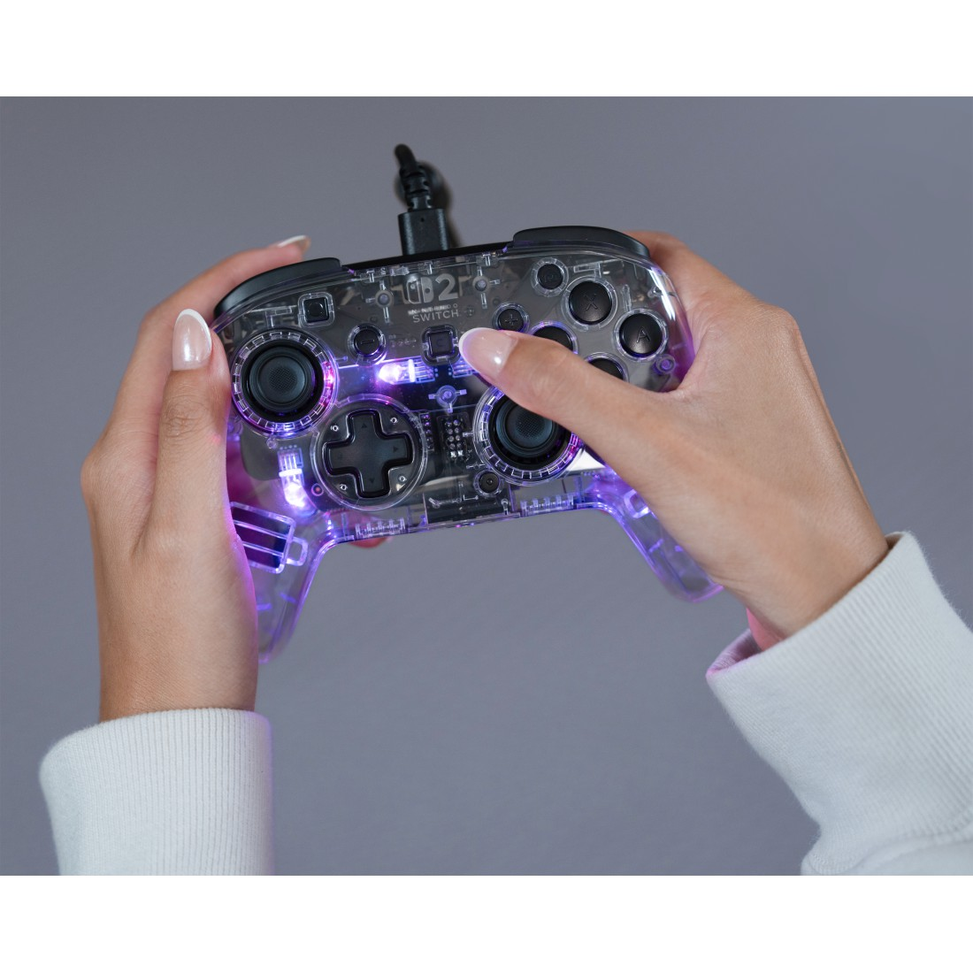 Hände halten eine transparente, beleuchtete Spielekonsole mit lila Lichtern.