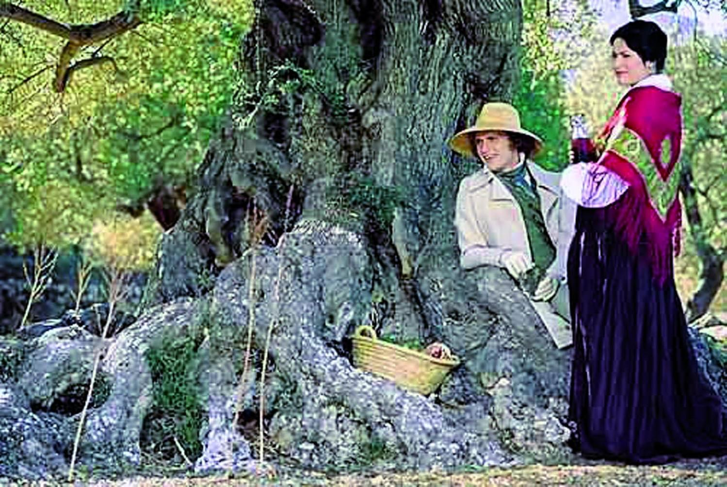 Ein Mann mit Hut und eine Frau in einem roten Schal sitzen neben einem Baum.