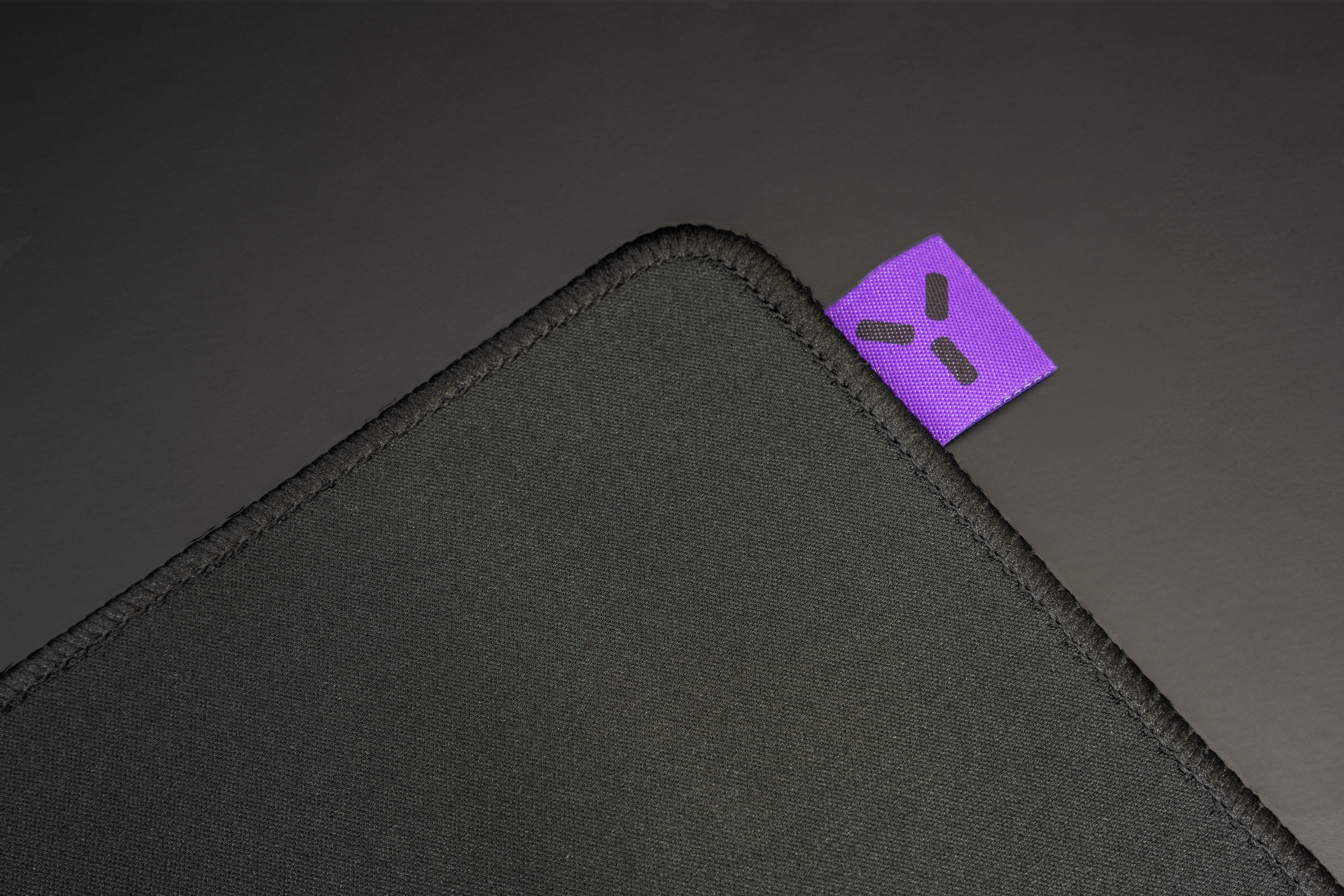 Czarny róg podkładki pod mysz z fioletową metką i czarnym symbolem.