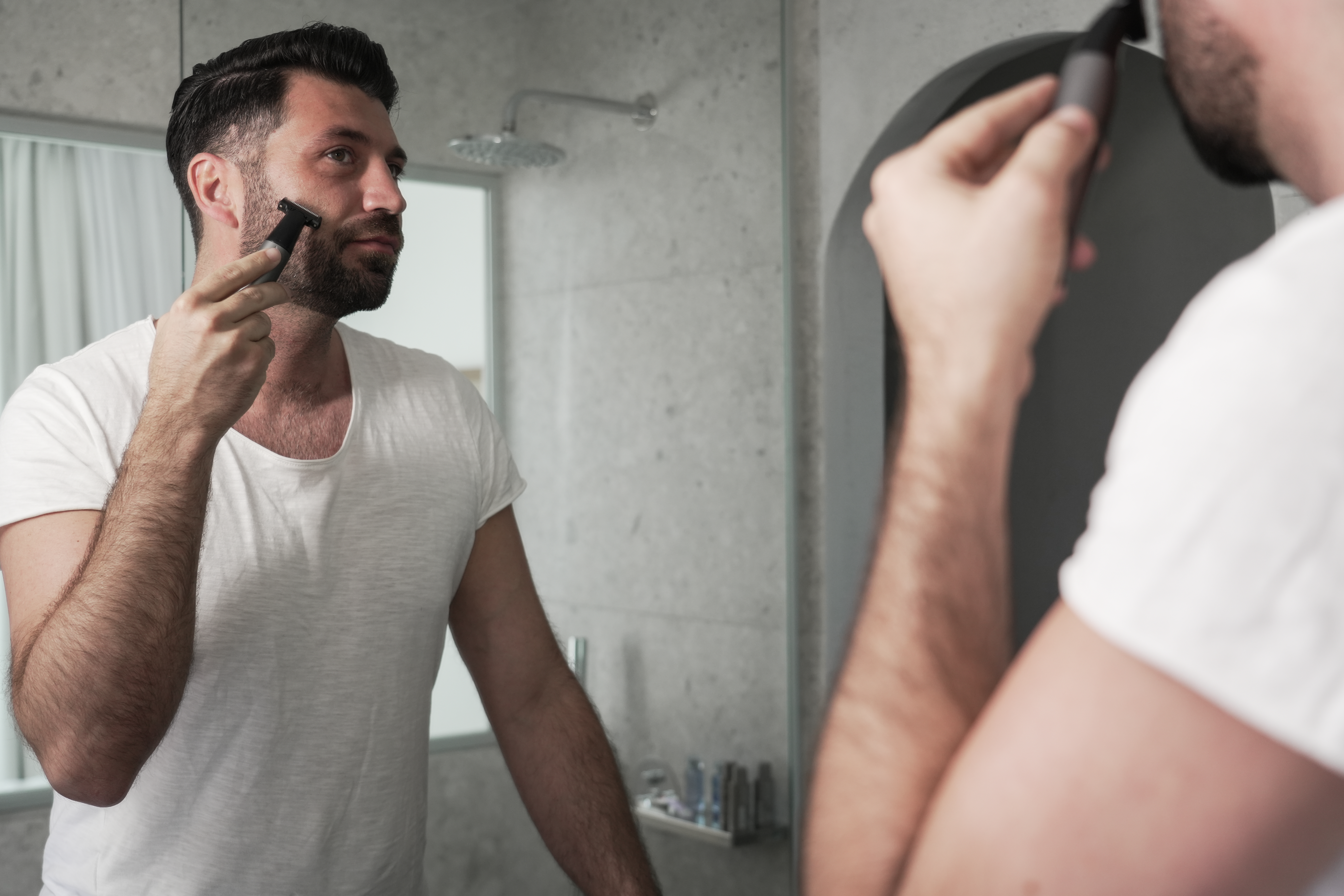 Mężczyzna goli twarz w lustrze trymerem.